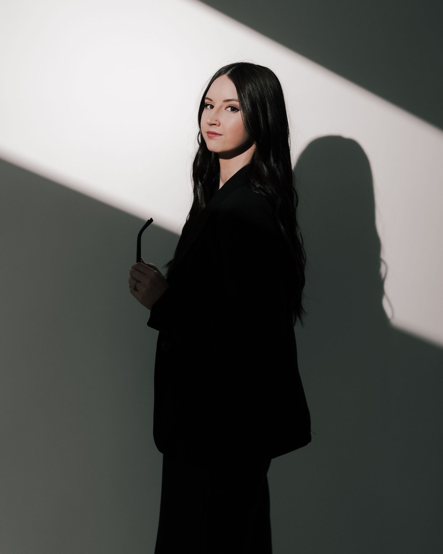 Dramatic portrait in contrasting light with dark silhouette against white wall creating striking shadows and depth.