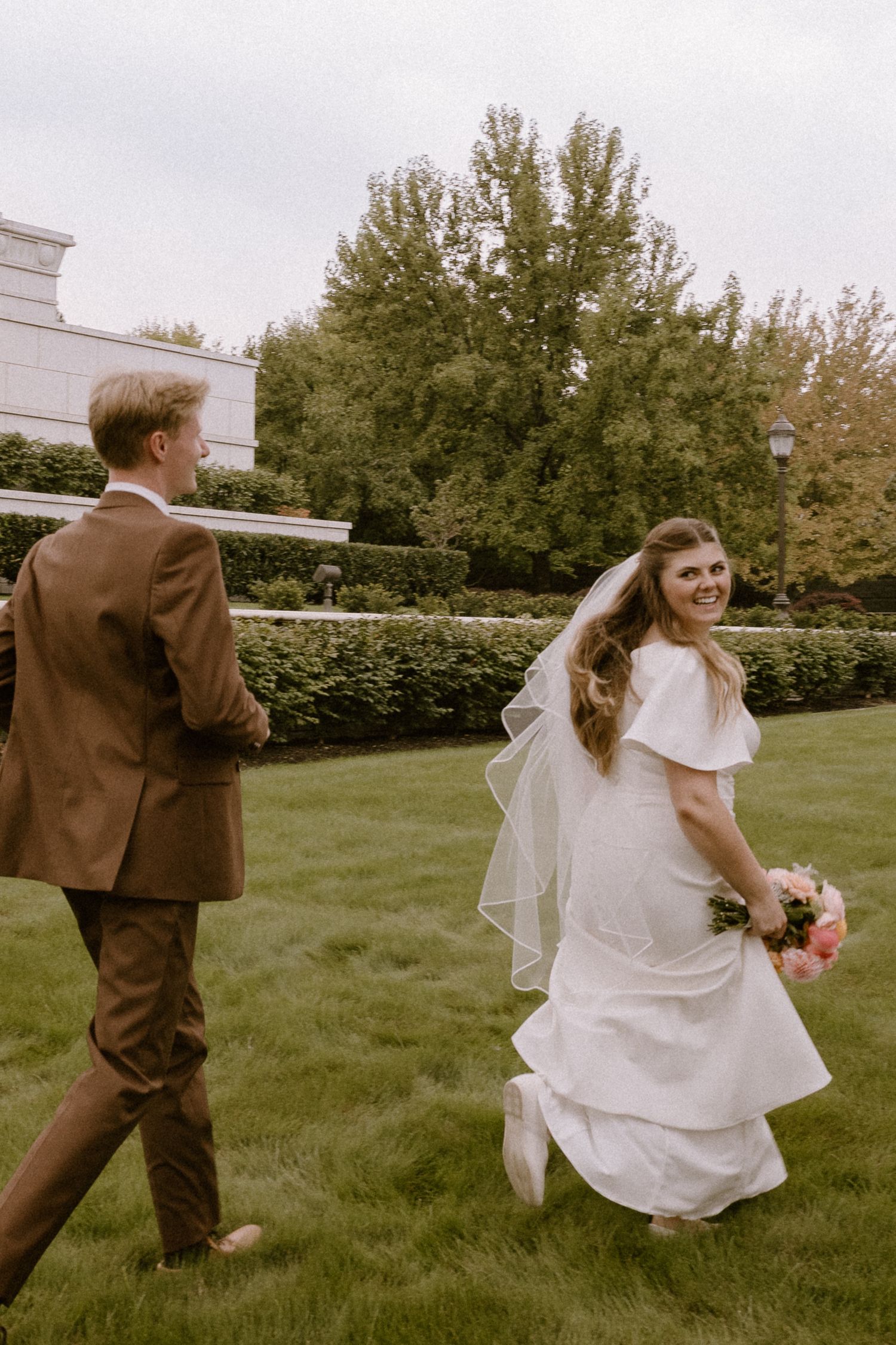 A sequence of three photos showing a couple in wedding attire playfully running and dancing on a grassy lawn.