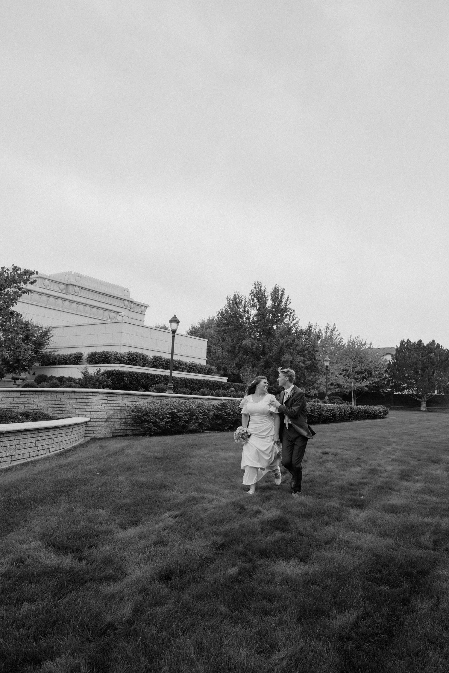 Black and white photo series shows couple walking up grassy hill with modern building in background.
