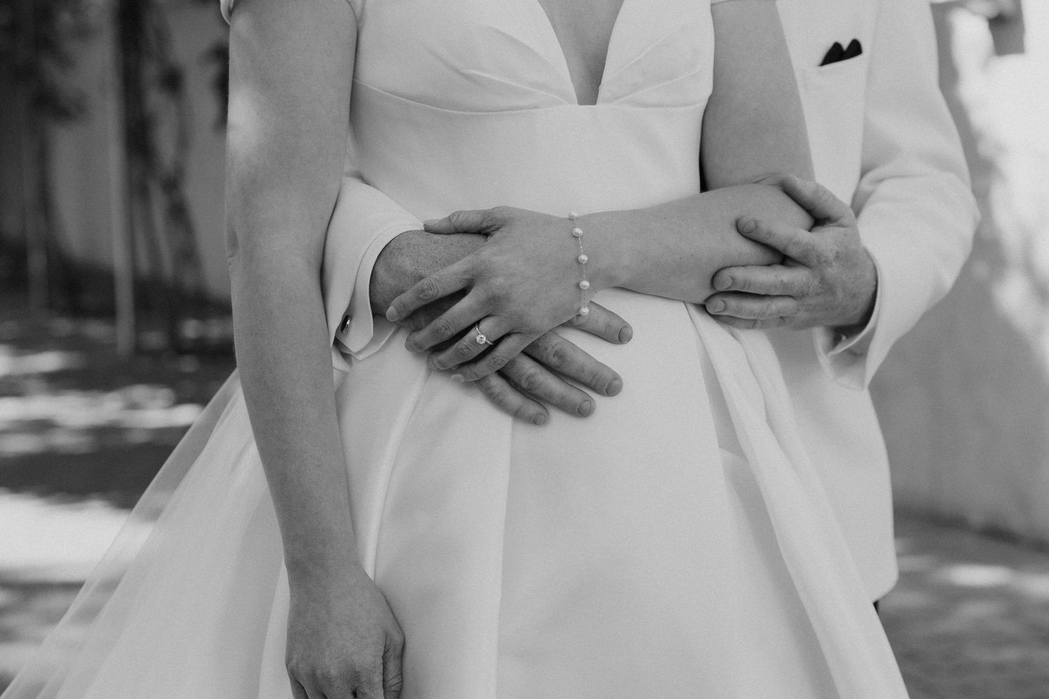Black and white close-up photo of hands embracing around a white wedding dress waist.