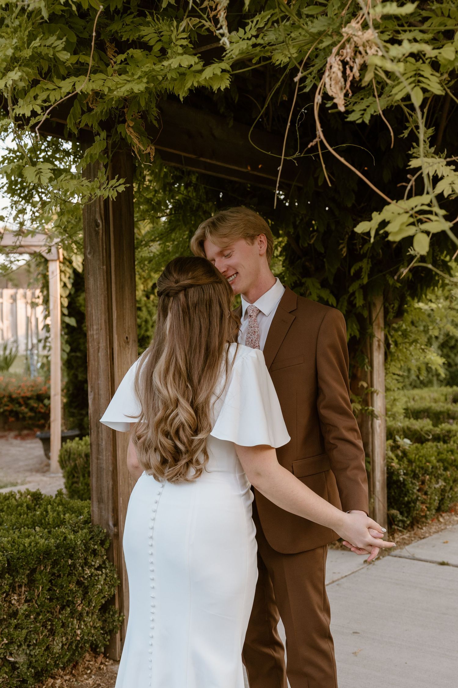 A couple shares a tender moment under green foliage in a romantic outdoor setting.