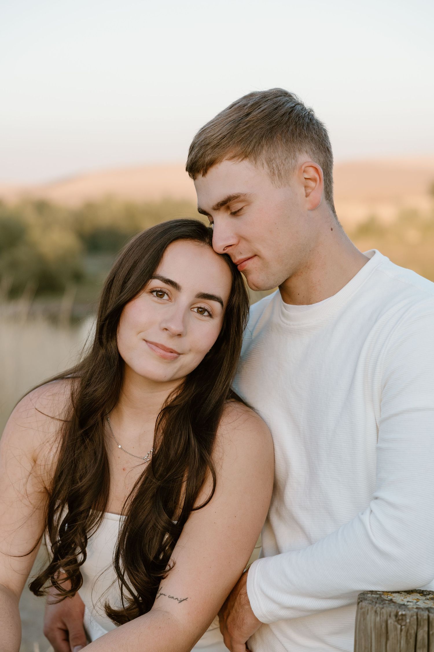 A romantic couple embraces during golden hour sunset in a natural outdoor setting.