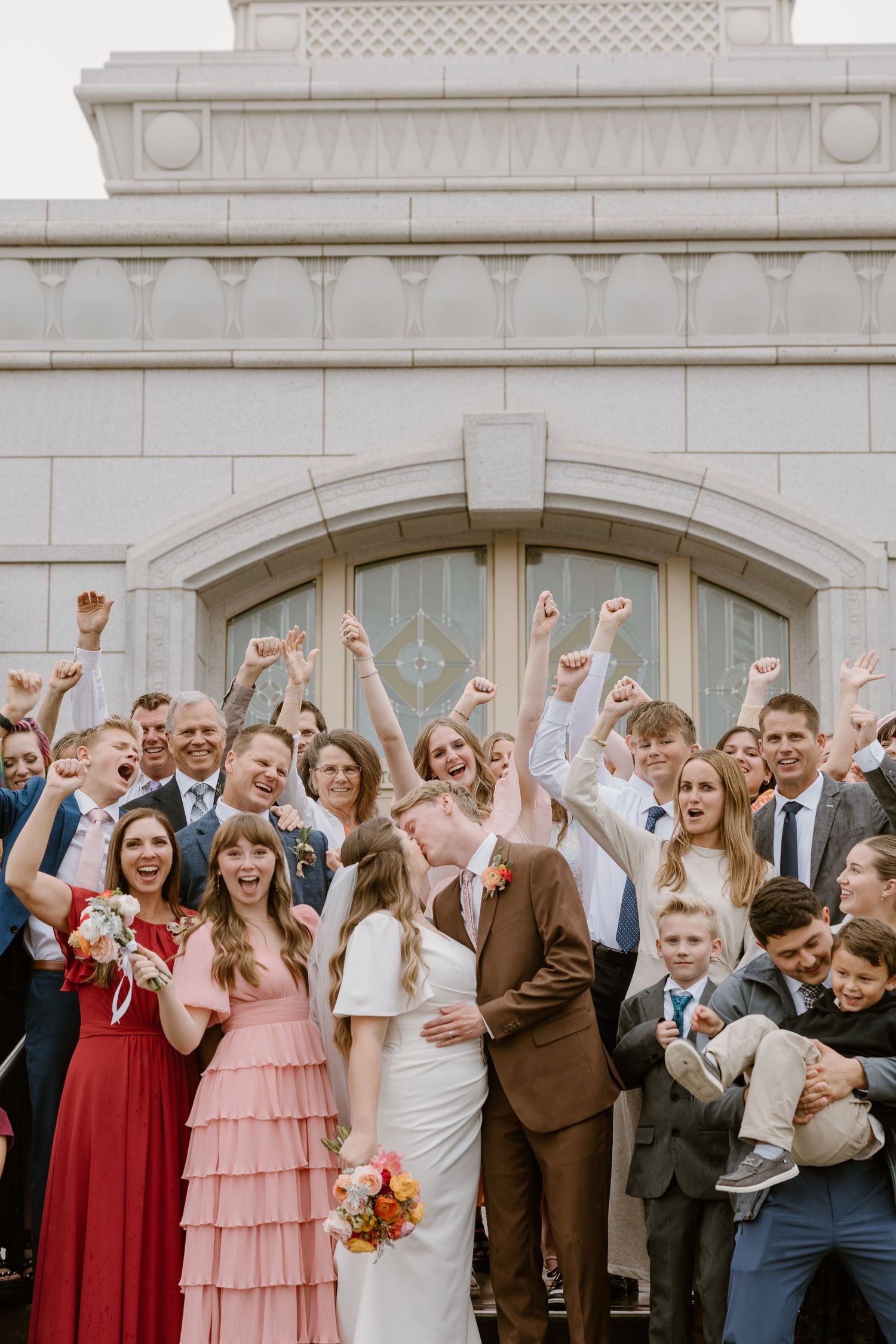 A joyful wedding party celebrates with raised arms and cheers on the church steps.