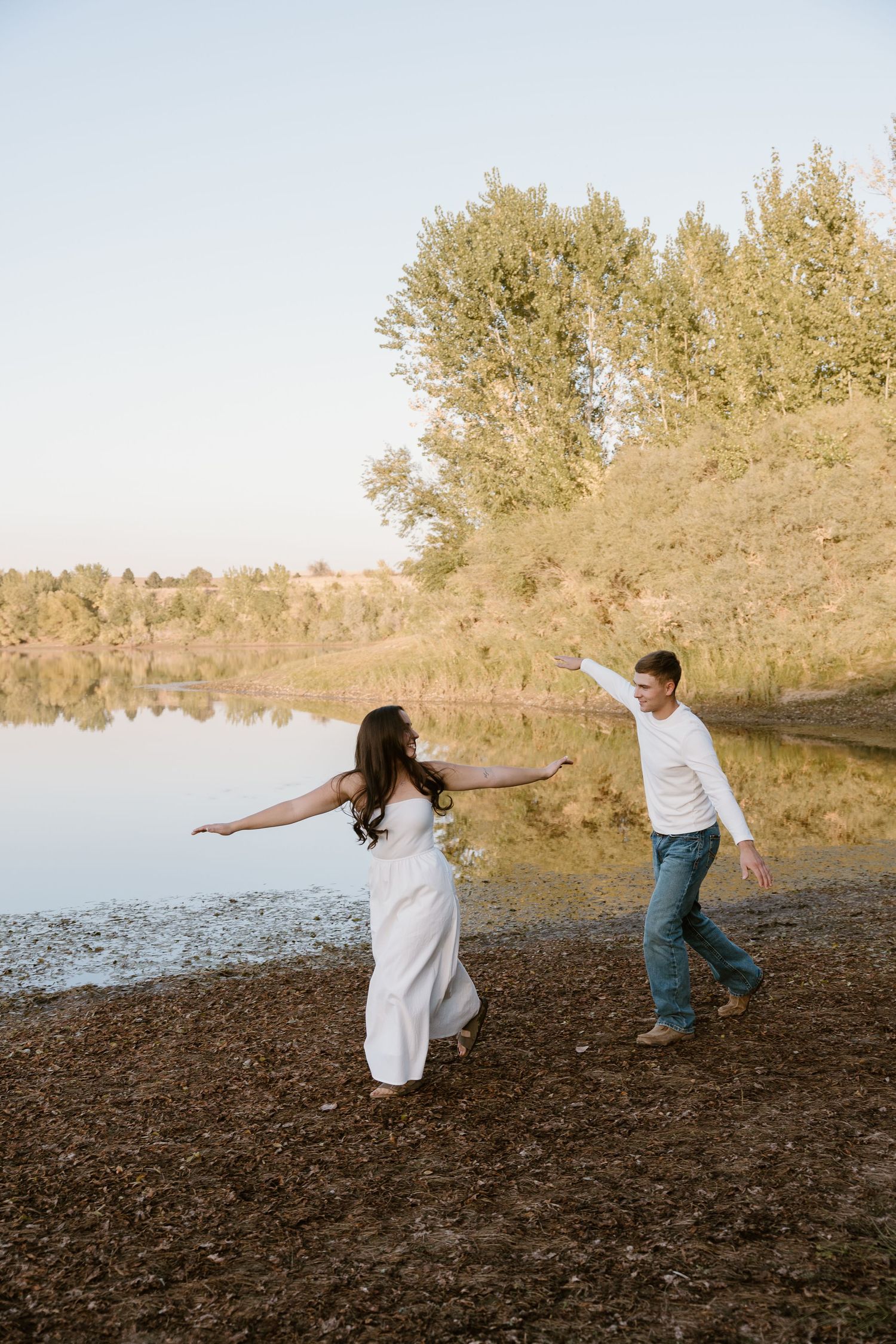 Two people dance playfully together on a rocky lake at sunset with trees in the background.