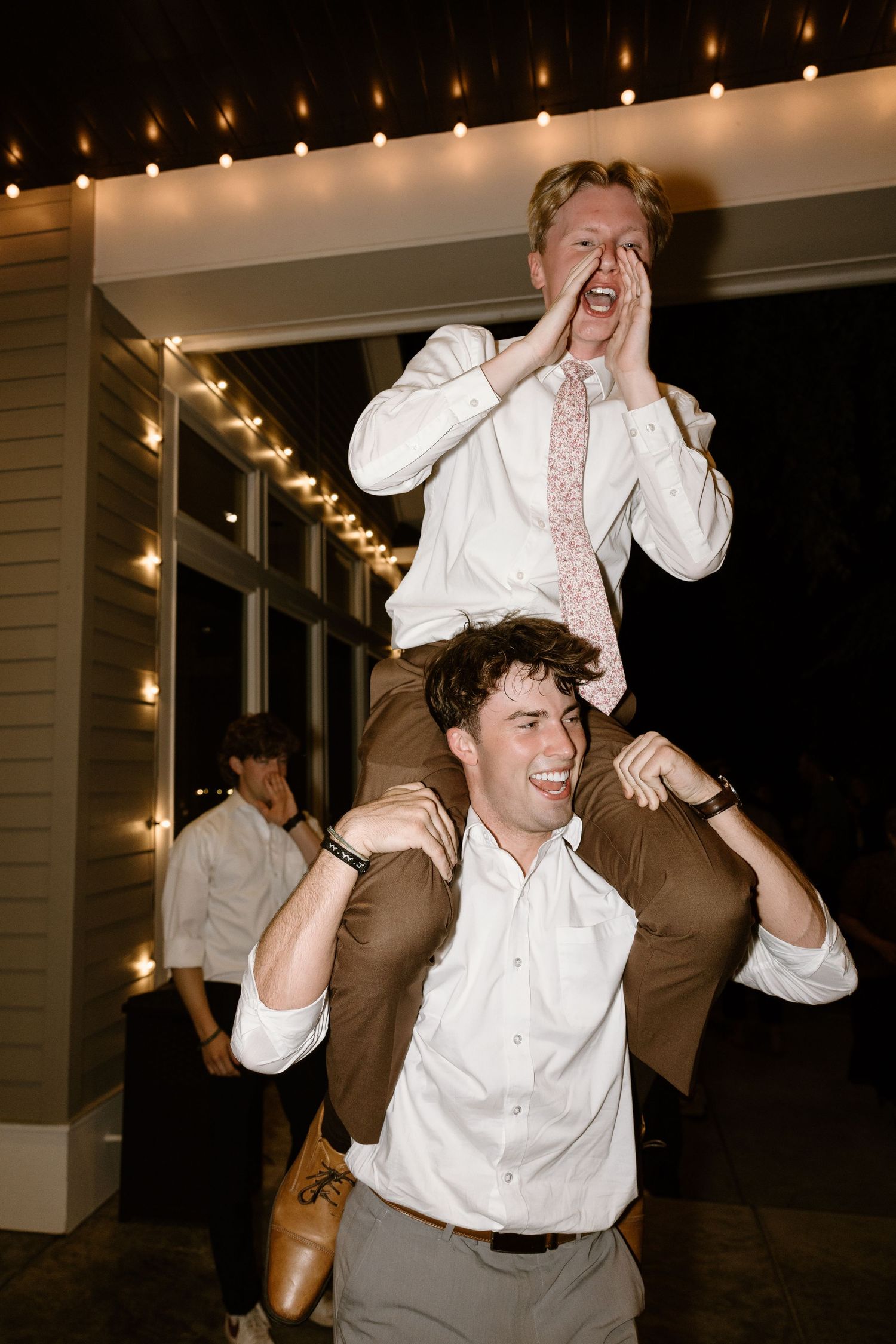 Wedding guests dance energetically on the dance floor under warm string lights at an evening reception.