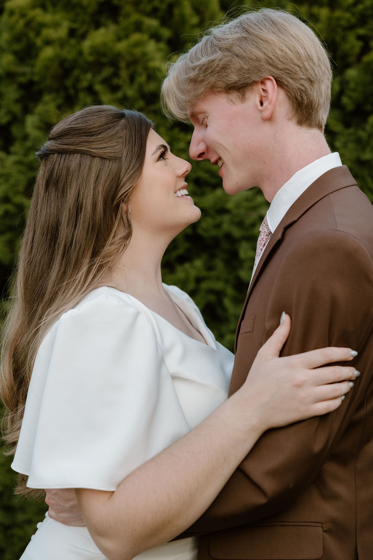 A couple in white and brown attire share romantic moments in a series of outdoor portraits against greenery.