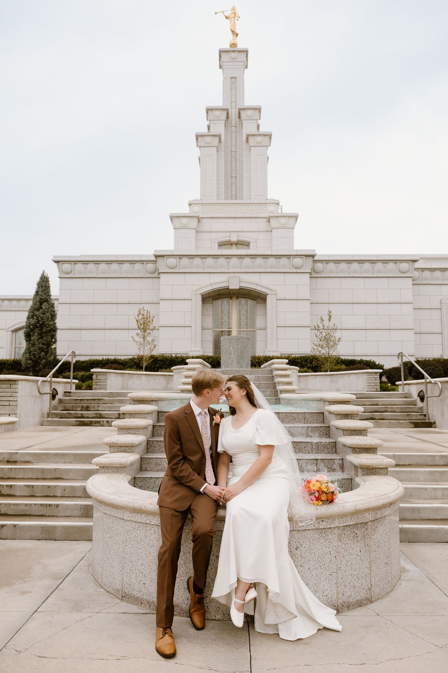 A couple shares romantic moments in front of a white stone Mormon temple on their wedding day.