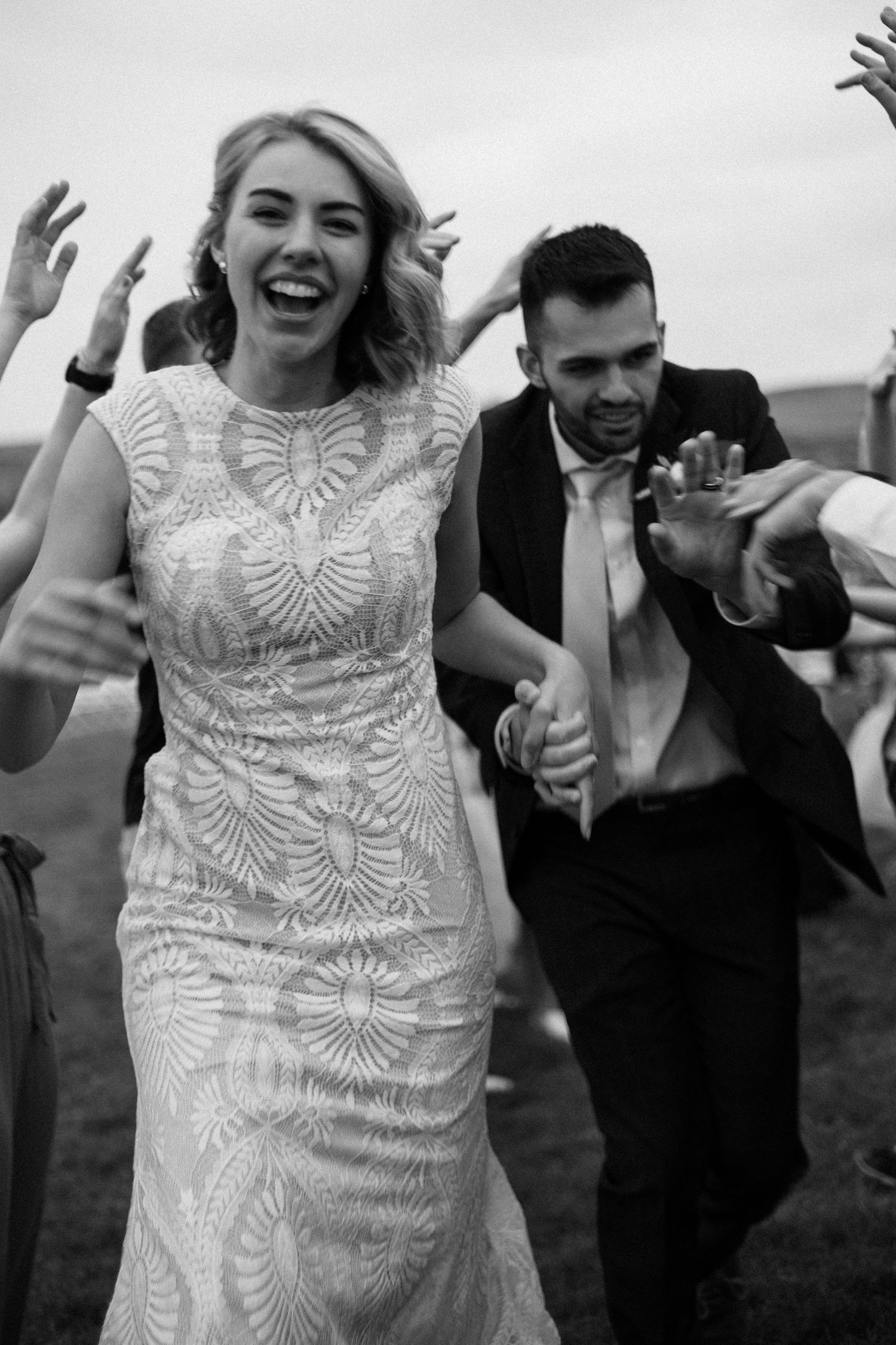 A sequence of black and white photos showing a bride in a detailed lace dress dancing joyfully at an outdoor wedding.