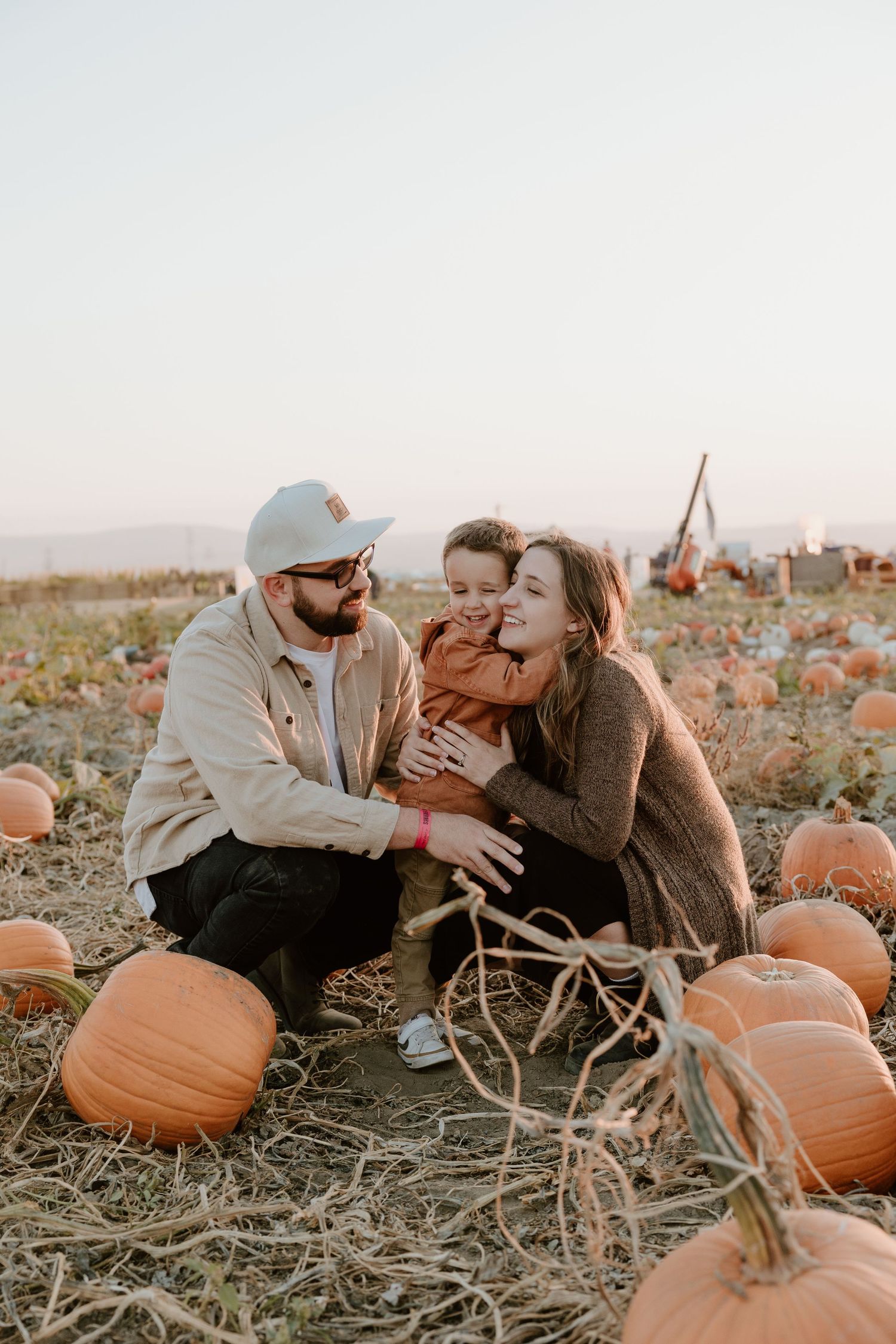 A family shares joyful moments together in a rustic pumpkin patch during golden hour sunset.