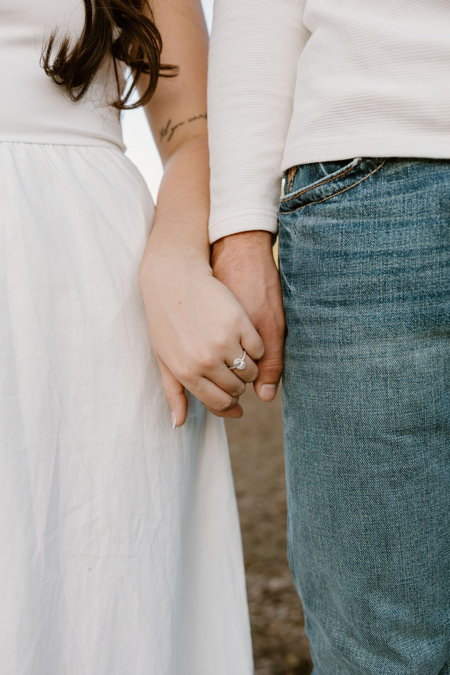 Close-up view of hands wearing rings against white dress and denim jeans backdrop.