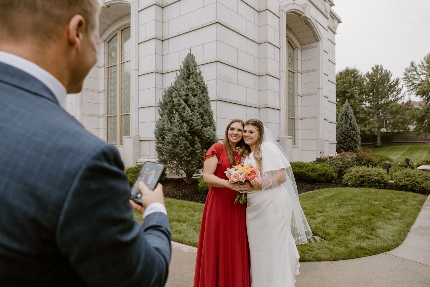 Couple in formal attire embracing outside an elegant white stone building during a wedding photo session.