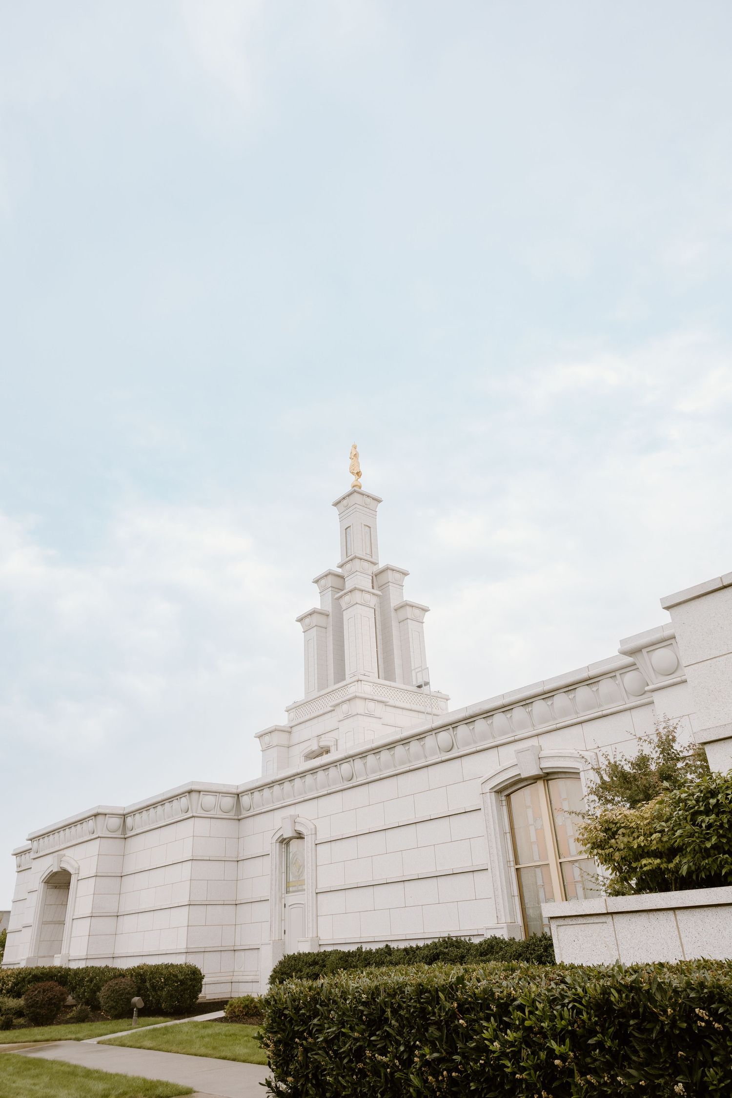White marble Mormon temple with spires and manicured hedges photographed from different angles against cloudy sky.