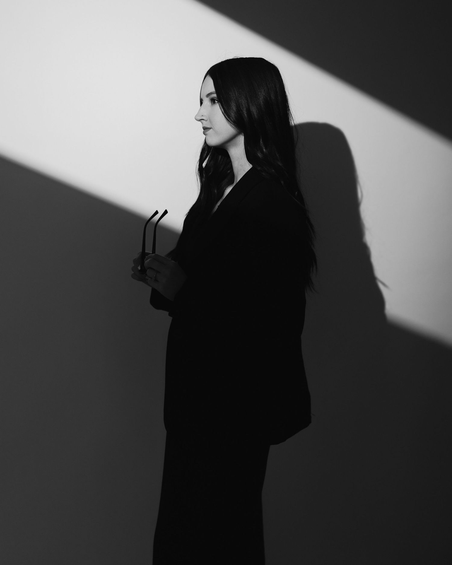 Dramatic black and white portrait with a striking diagonal shadow cast on the wall behind a person in dark clothing.