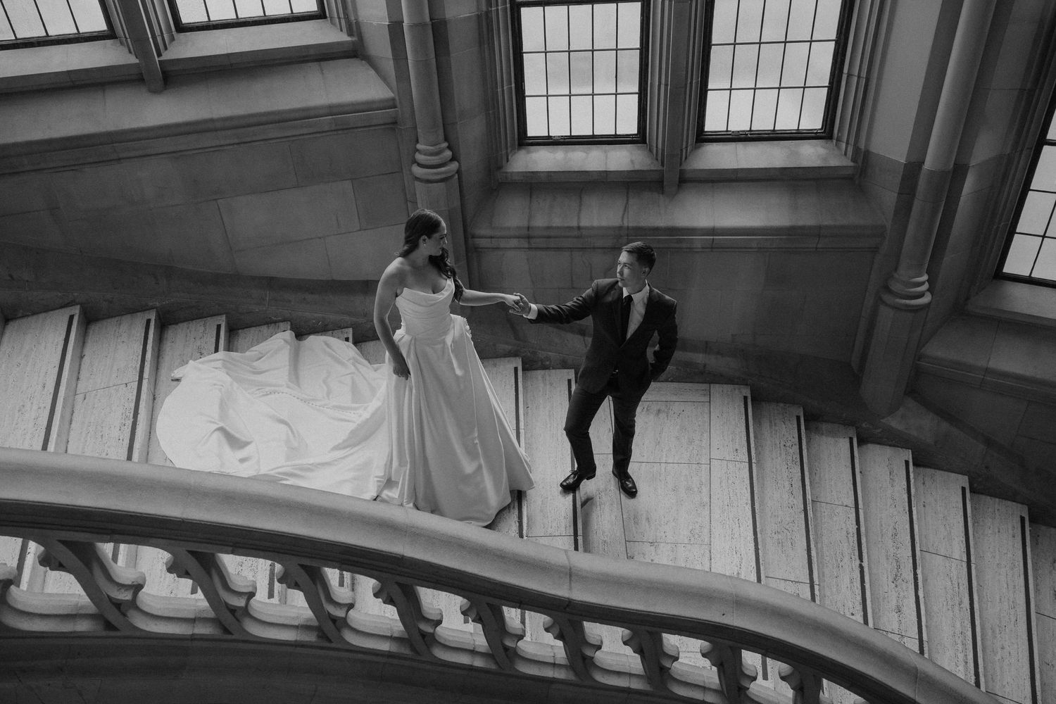 A black and white photo shows a bride and groom descending an elegant staircase in the Suzzallo Library at UW in Seattle, Washington.