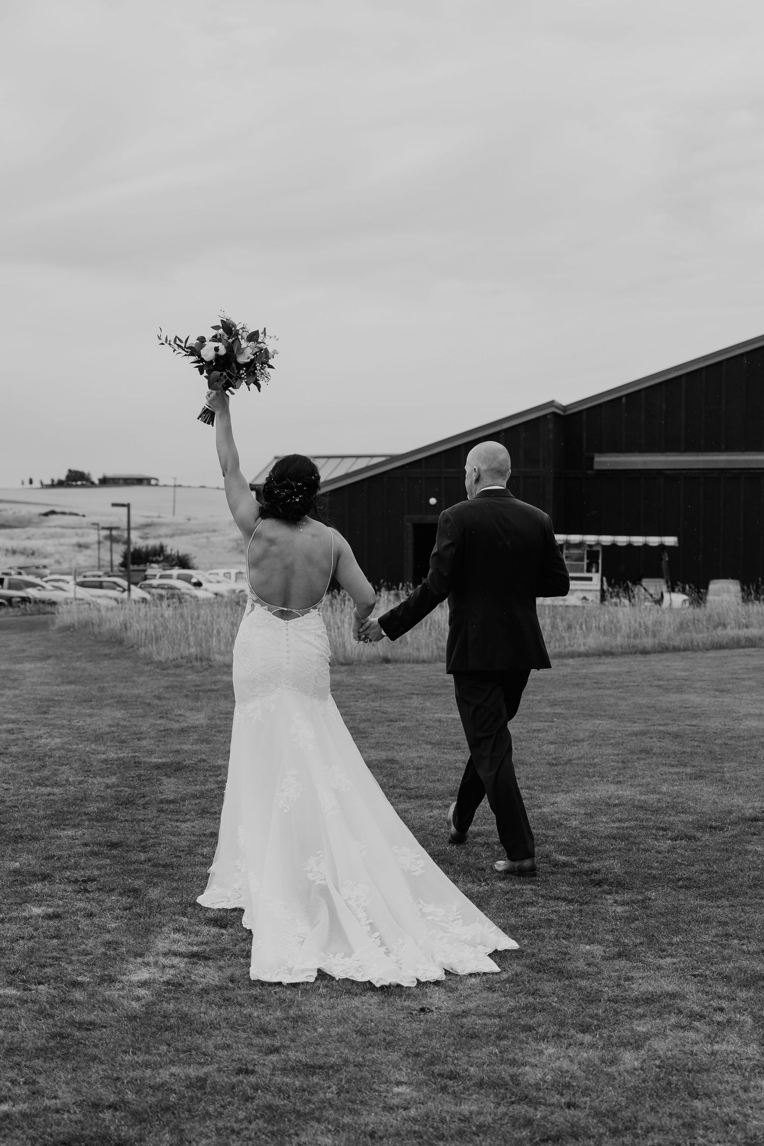 A black and white wedding photo showing a couple walking on grass with the bride holding a bouquet up in celebration.