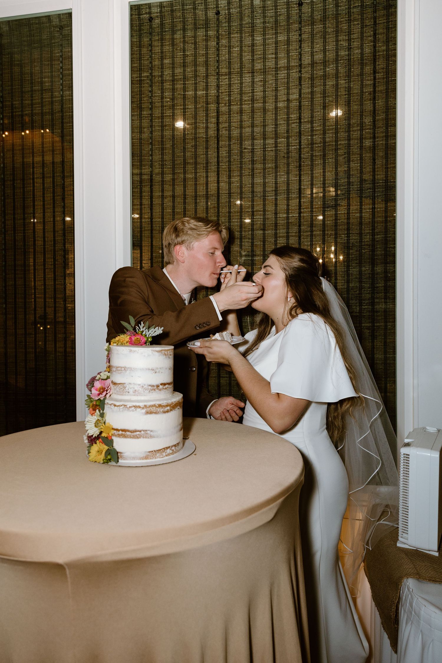 Newlyweds share a playful moment while feeding each other wedding cake at their reception.