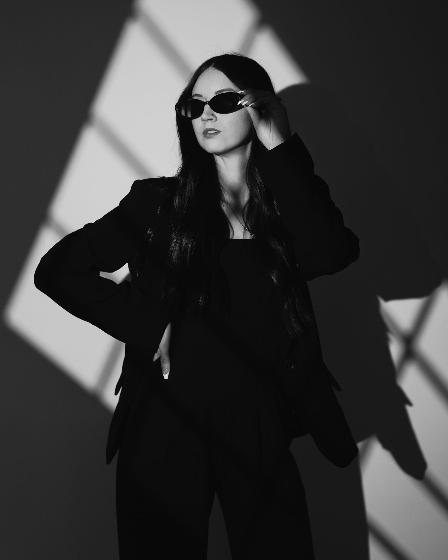 Dramatic black and white fashion portraits showing a woman in sunglasses and dark clothing posing against shadows.