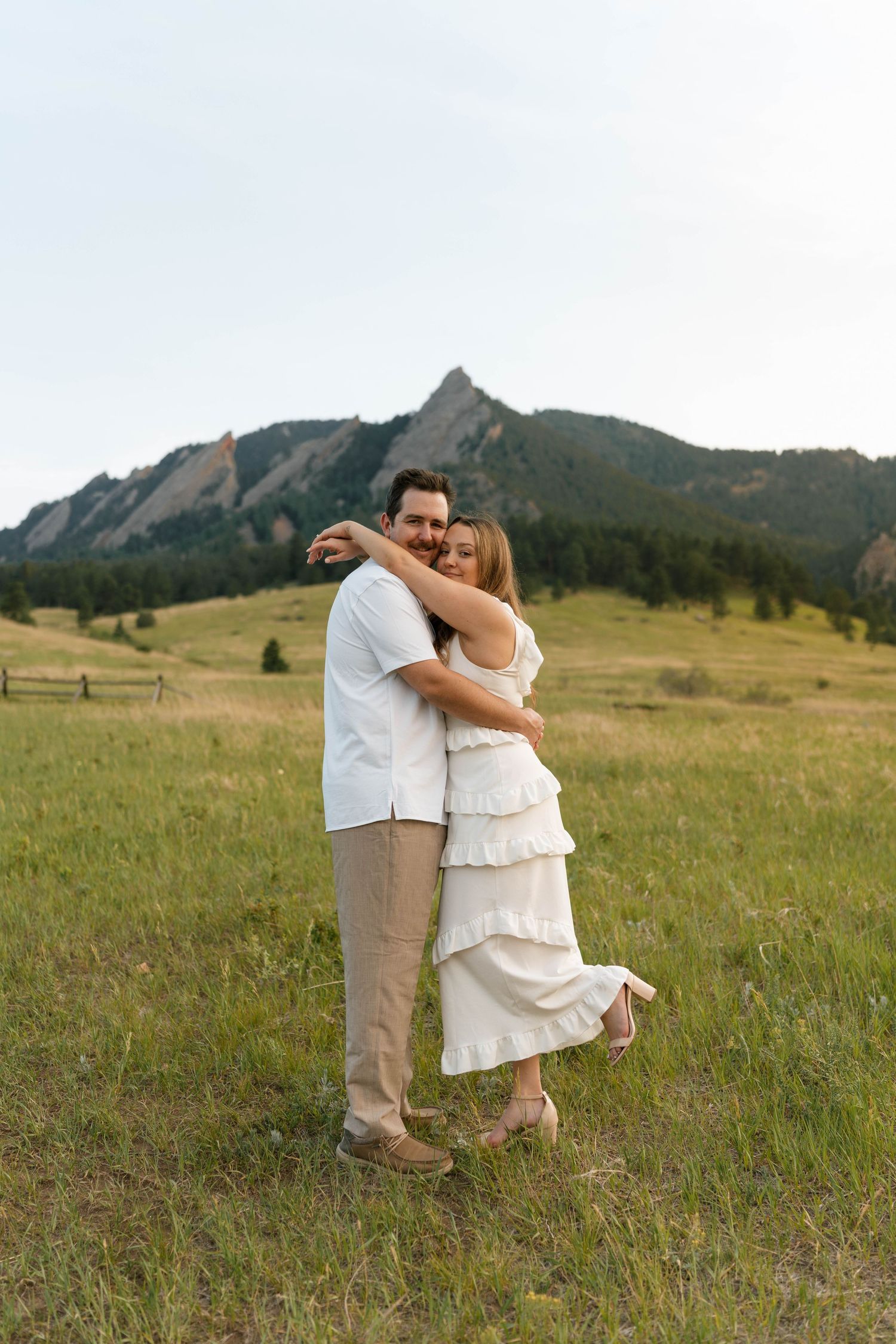 Couple embracing in a green field with the iconic Boulder Colorado Flatirons rock formations in background.