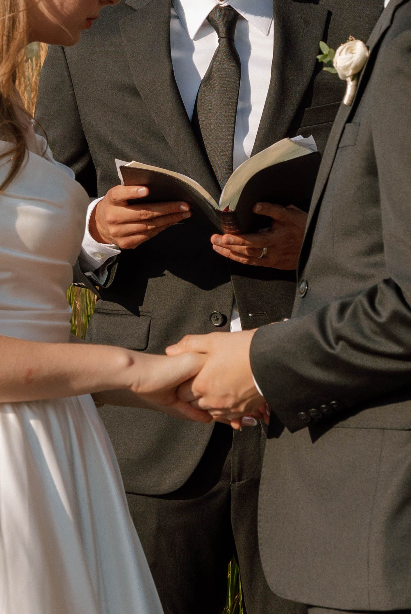 Close-up of hands holding a book during a wedding ceremony with formal attire.