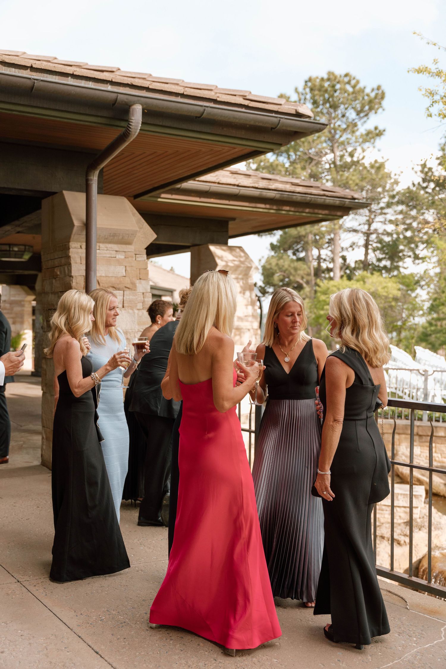 Wedding guests in formal attire gathered on an outdoor stone patio during reception celebrations.