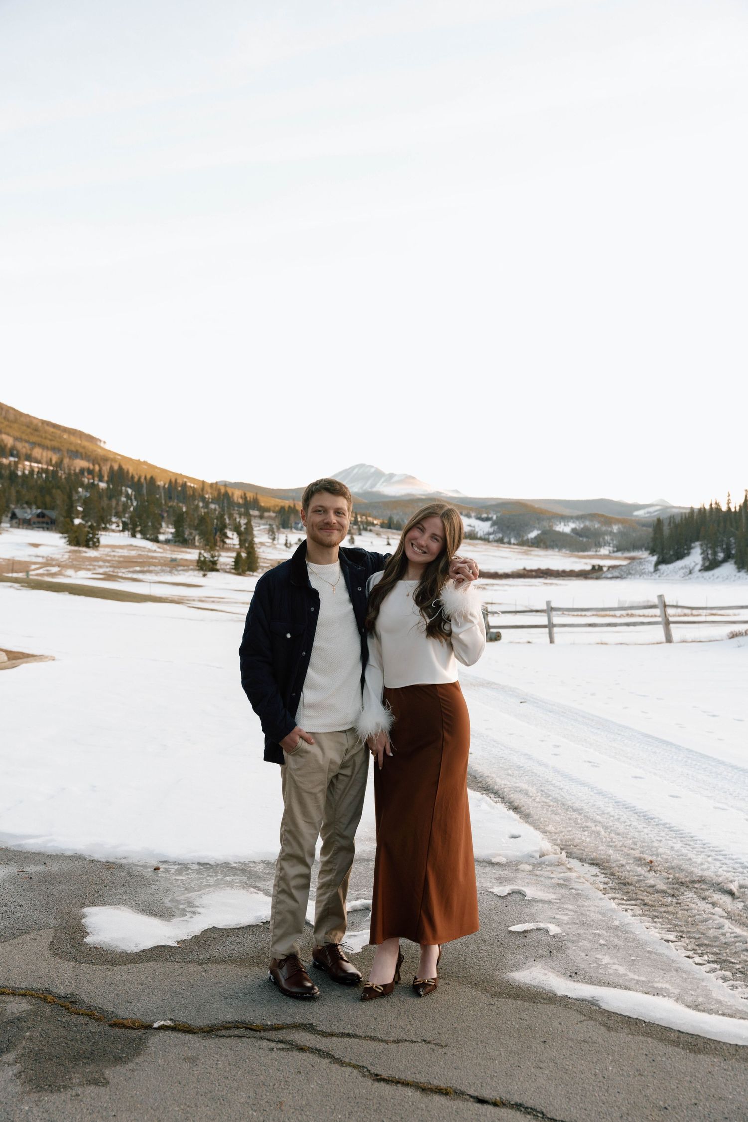 Couple enjoying a winter stroll along a mountain road with snow-covered landscape.