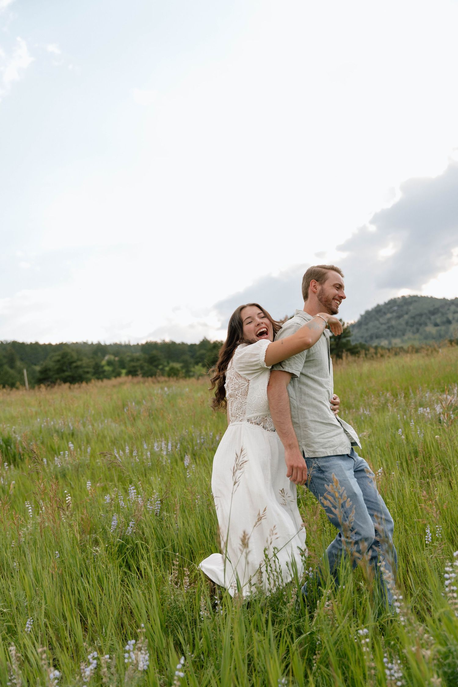 A joyful couple plays and laughs together in a scenic mountain meadow.