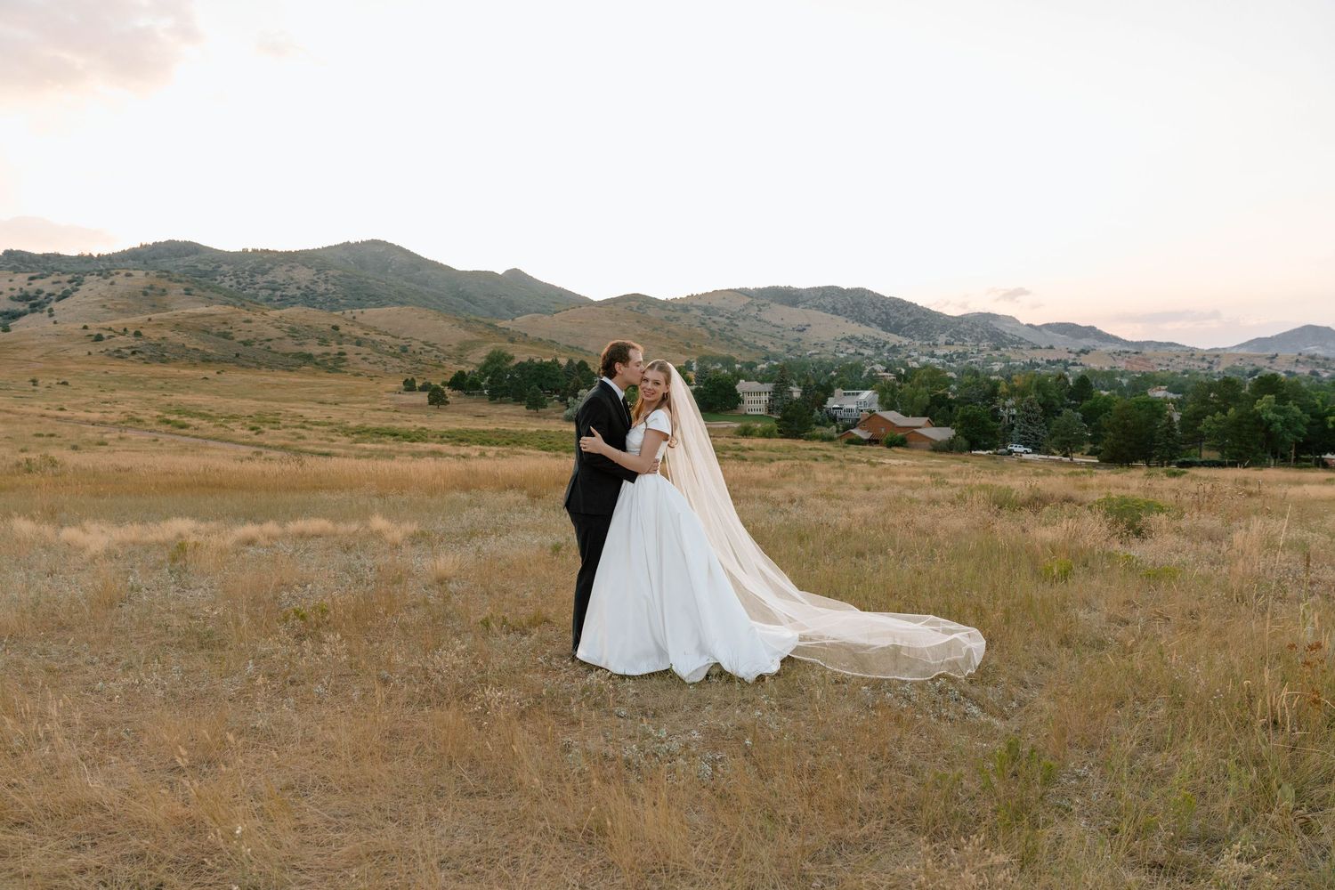 Scenic wedding photography in a vast golden field with mountains in the background.