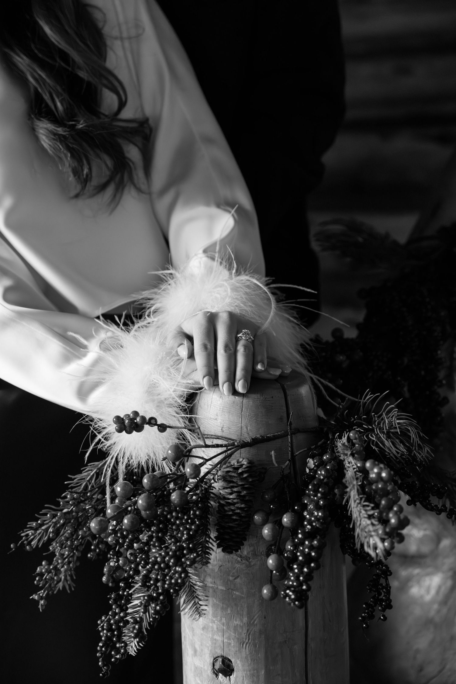 Black and white detail shot of hands arranging delicate feathers and berries.
