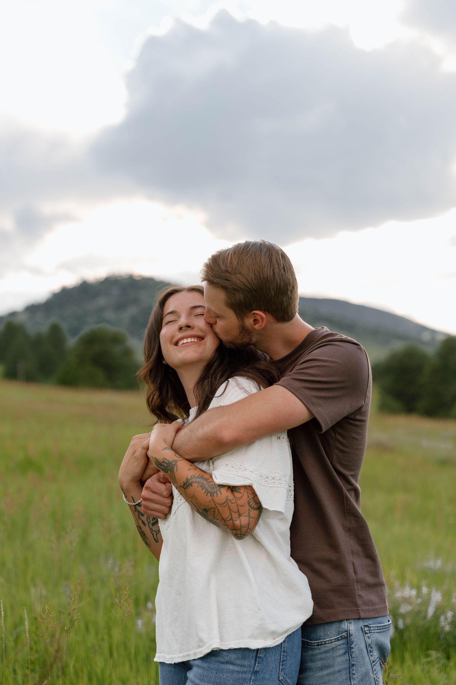 Joyful couple sharing a tender moment in a mountain field at dusk.