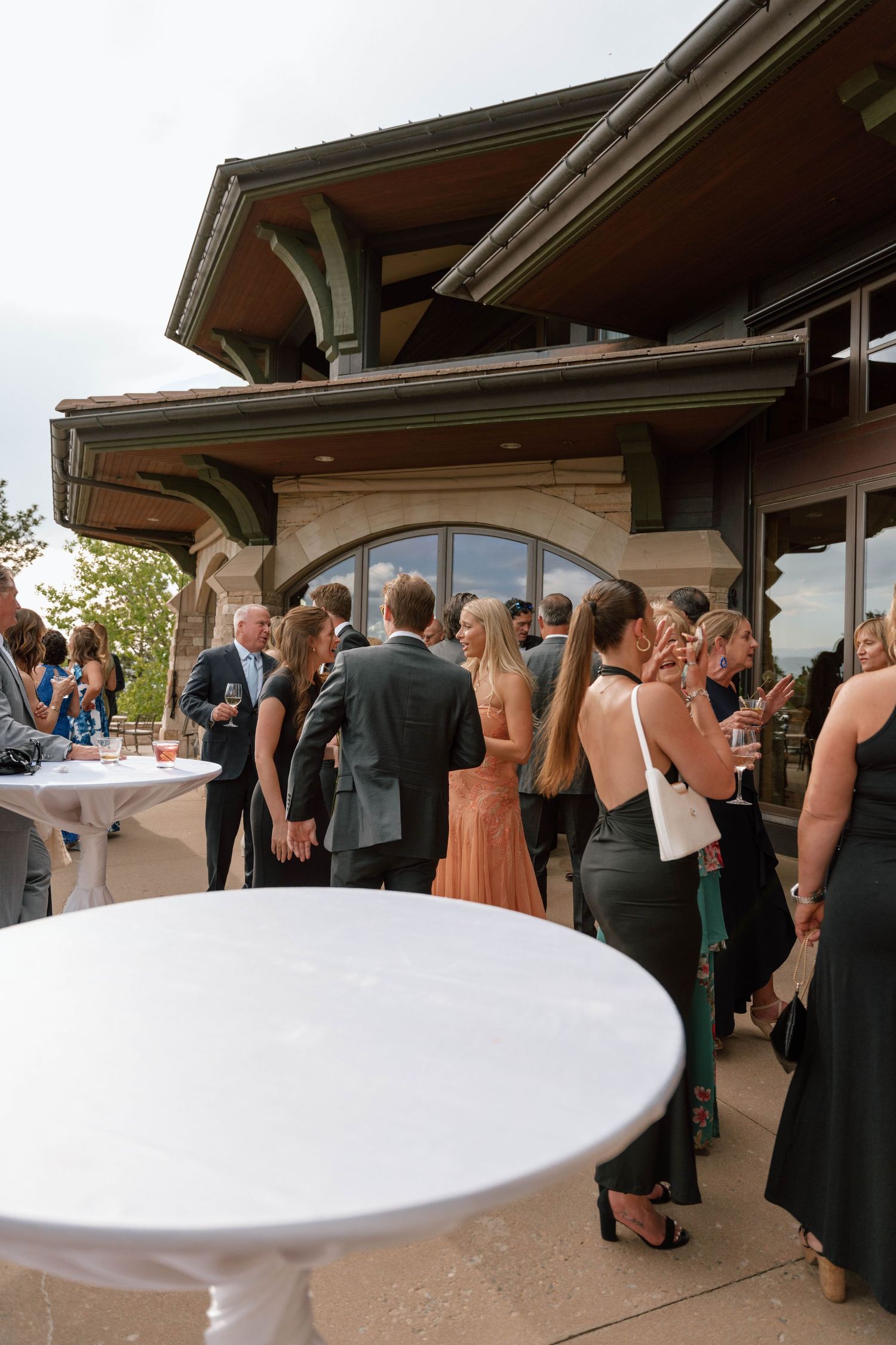 Wedding reception guests mingling around cocktail tables on an outdoor terrace.