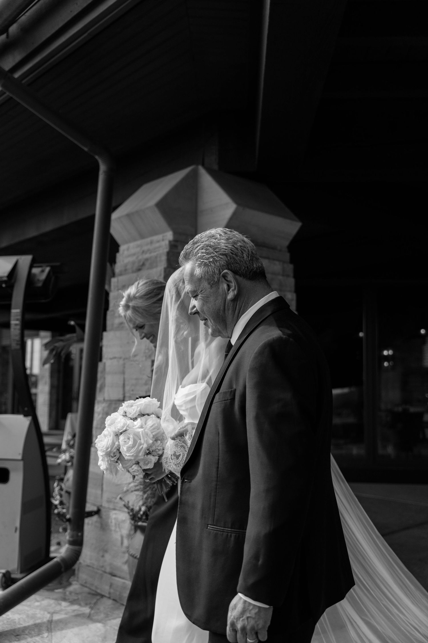 Black and white photo of a wedding couple walking through a covered stone archway.