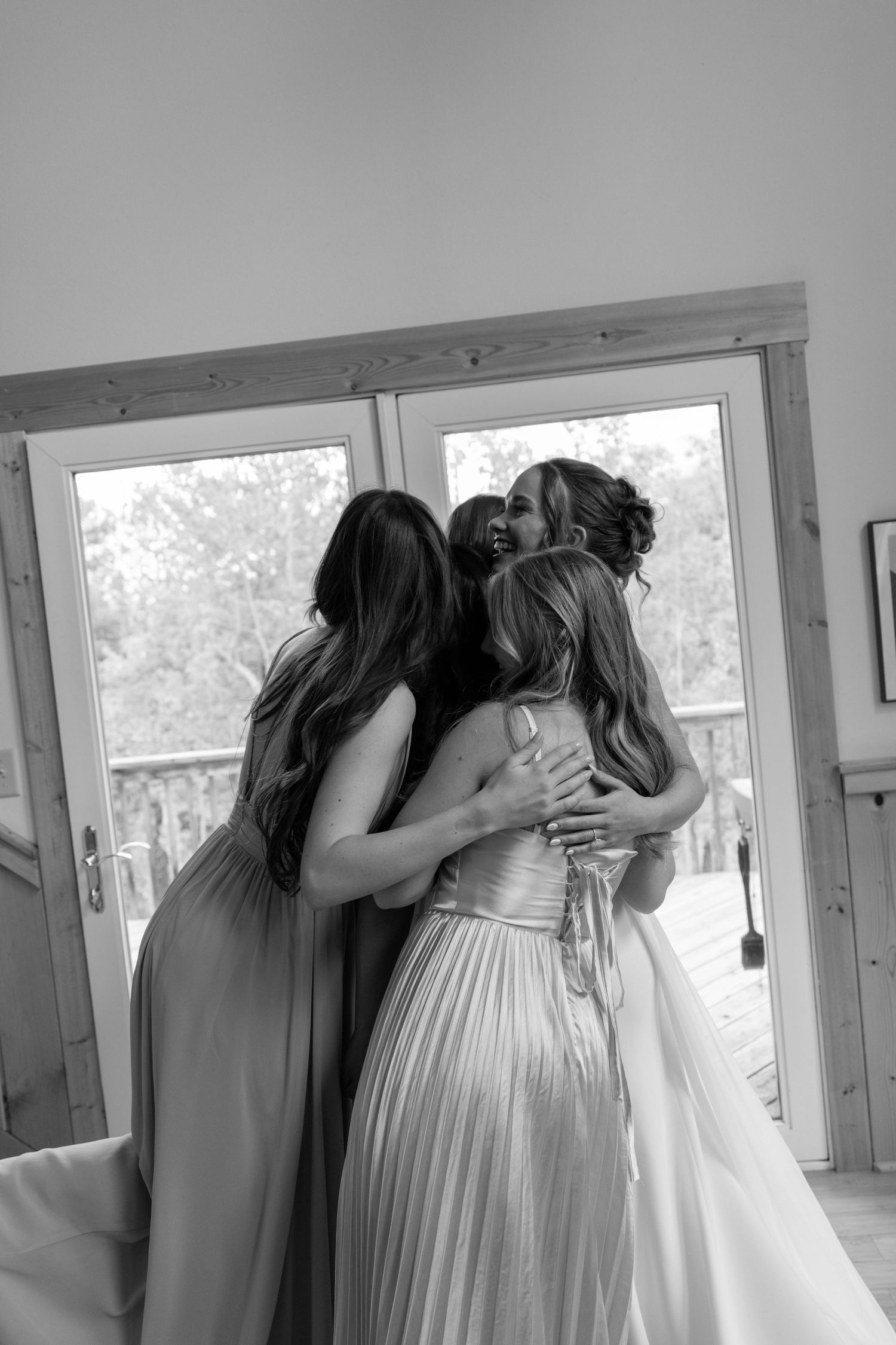 Black and white photo of bride being embraced by two bridesmaids before wedding ceremony.