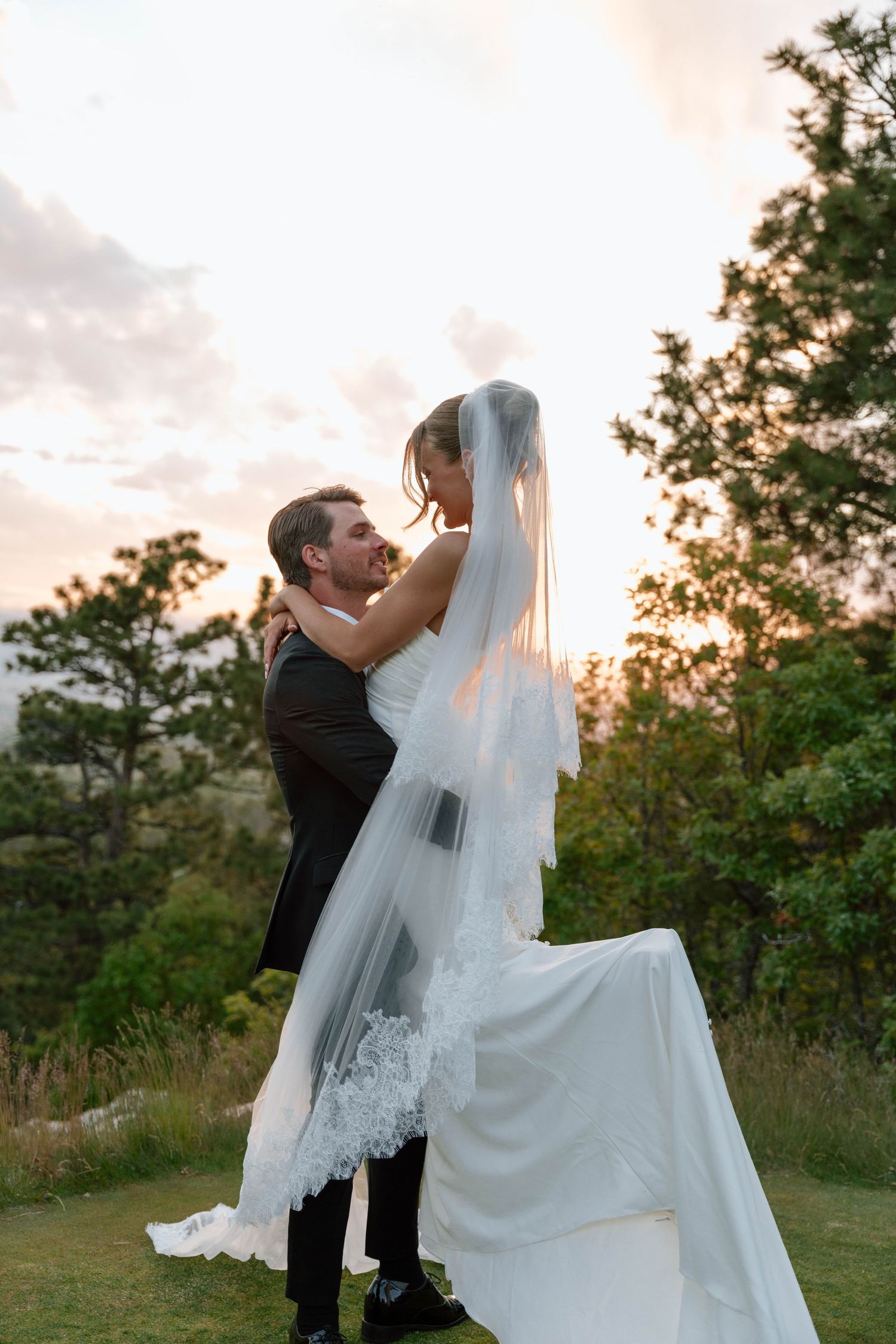 Couple shares playful moment with bride's veil during sunset wedding photoshoot.