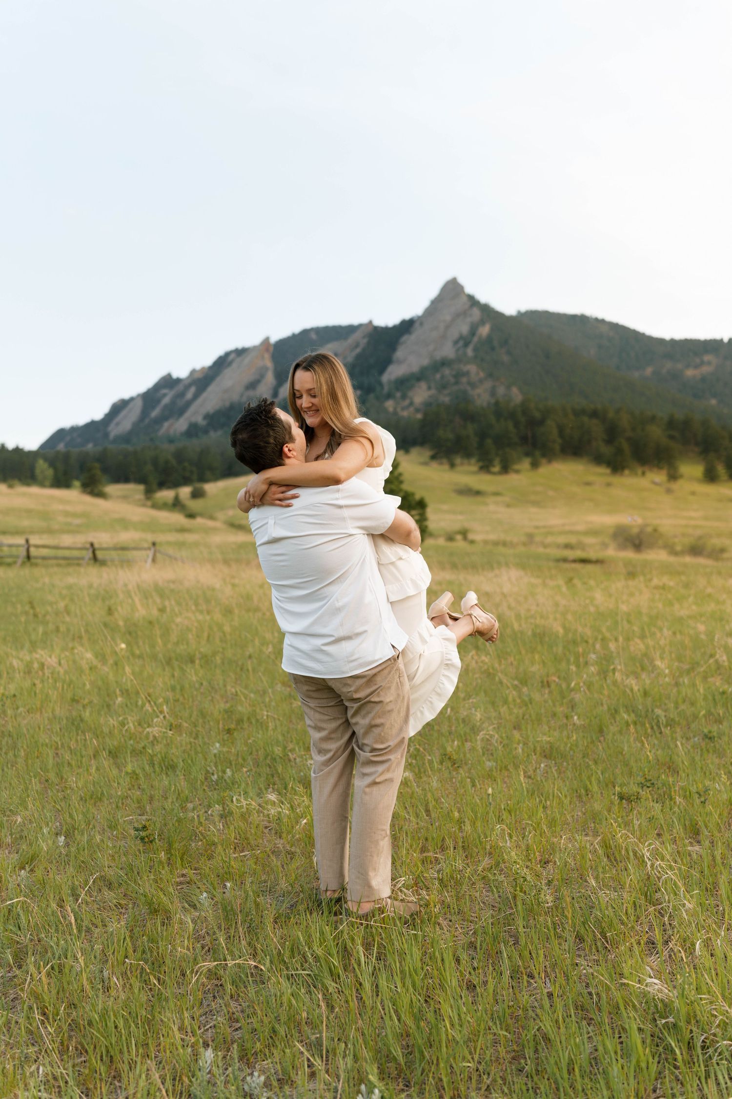 Couple embracing in a green meadow with the Flatirons mountains in Boulder, Colorado in the background.
