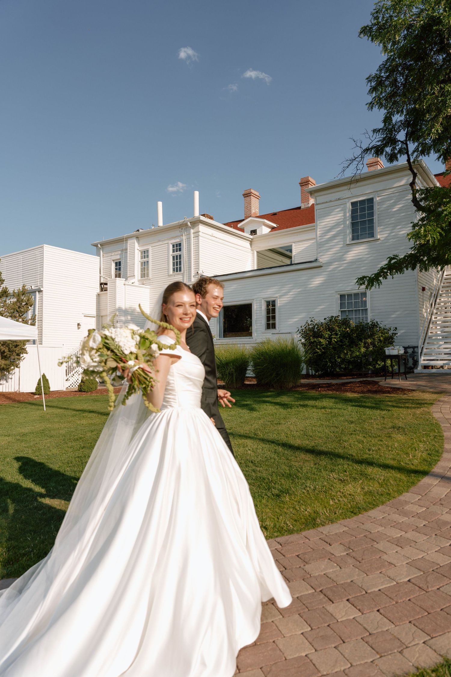 A newlywed couple joyfully exits their wedding ceremony in front of a classic white building.