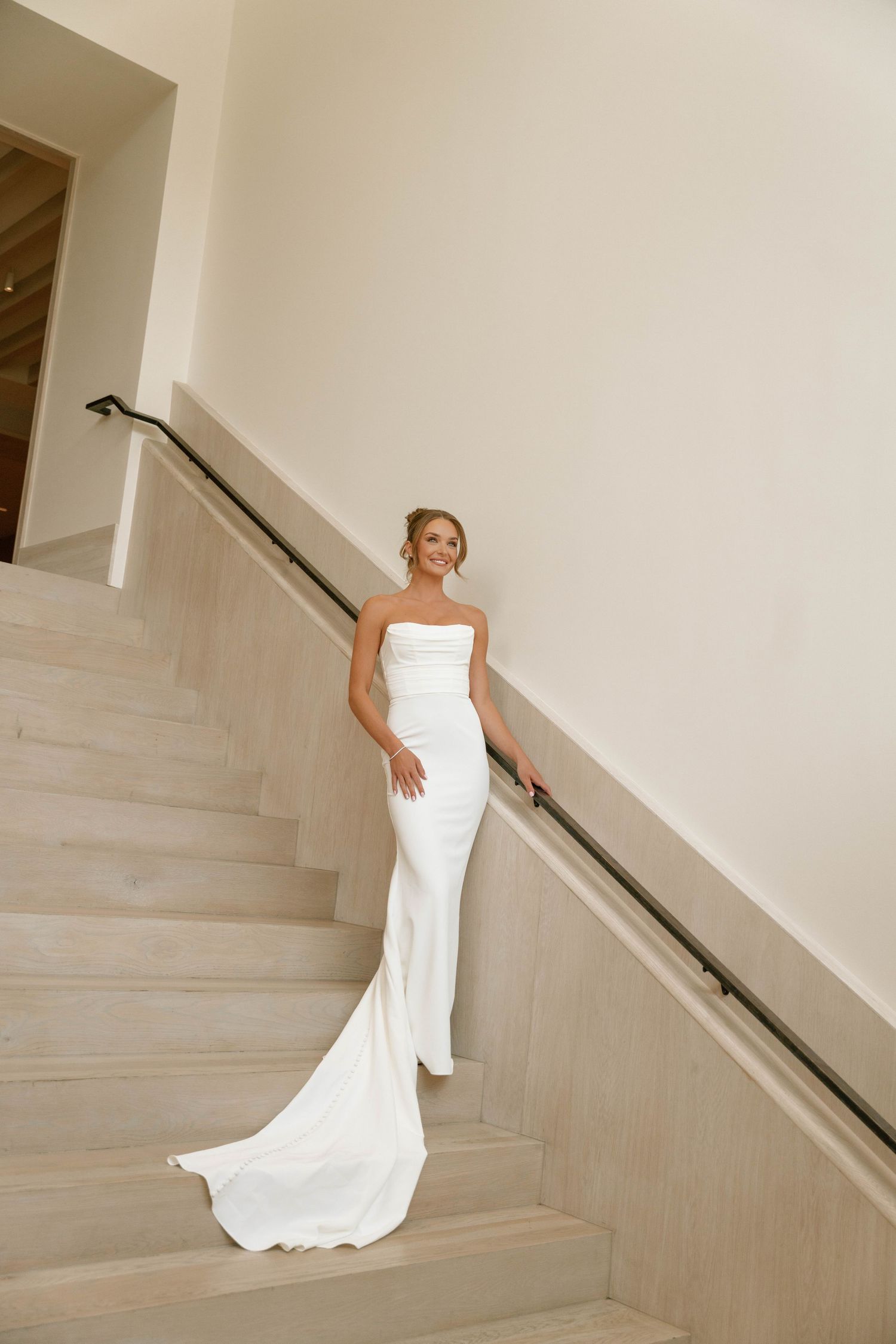 Bride in a strapless white mermaid gown with a train poses gracefully on elegant marble stairs.