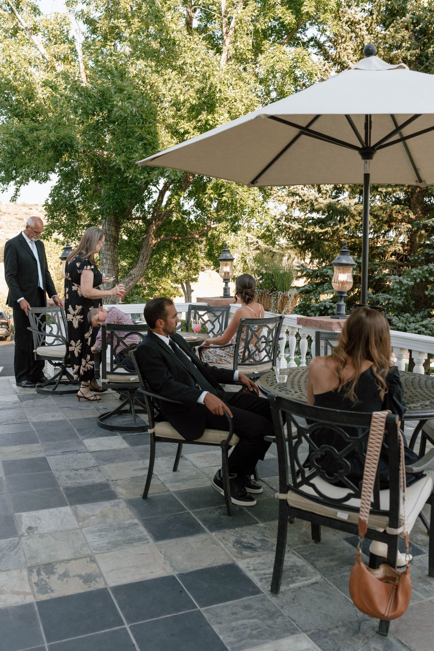 Guests relax on outdoor patio furniture under umbrellas at an elegant venue.