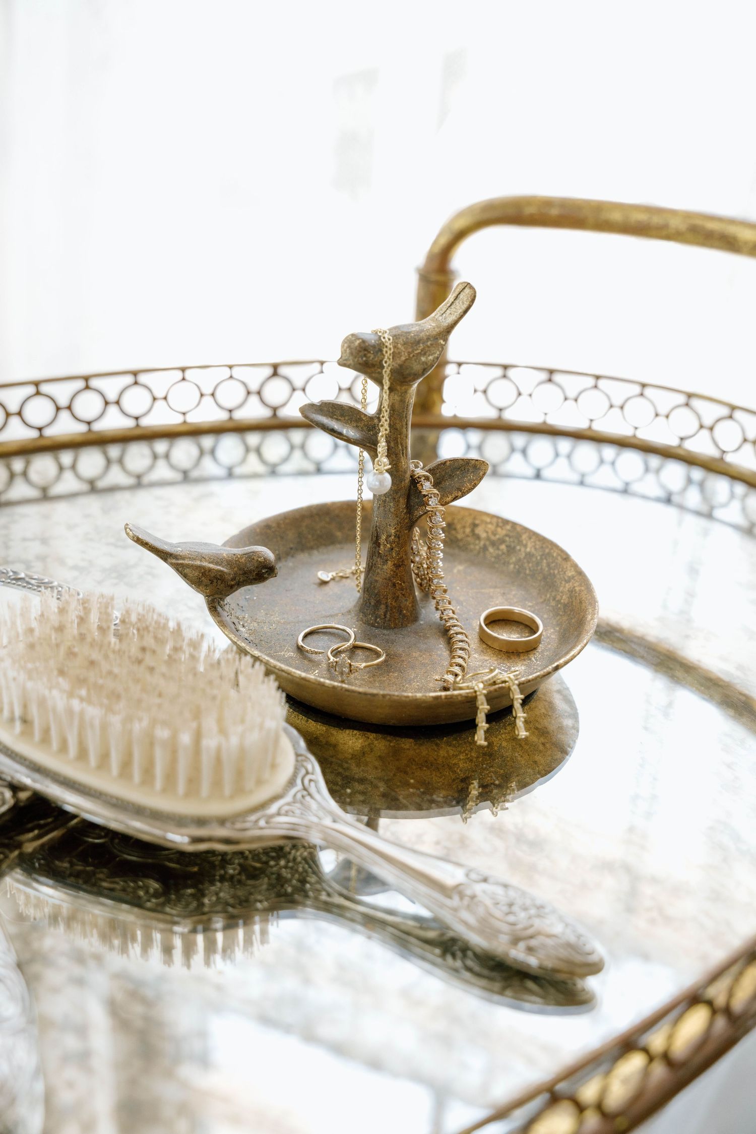 Vintage silver vanity tray with ornate ring holder and wedding rings displayed alongside an antique brush.