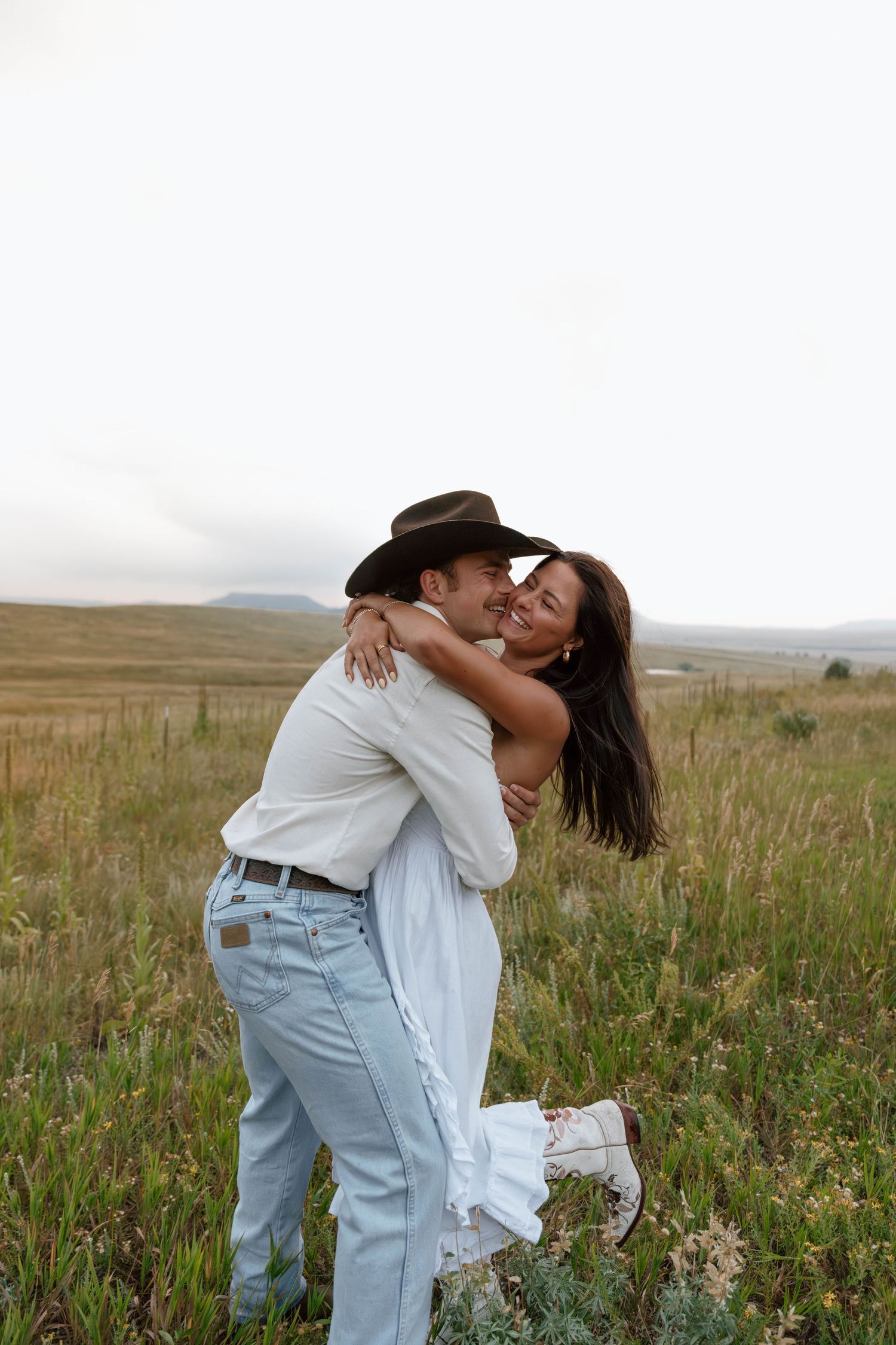 A joyful embrace in a mountain field with cowboy-inspired styling.