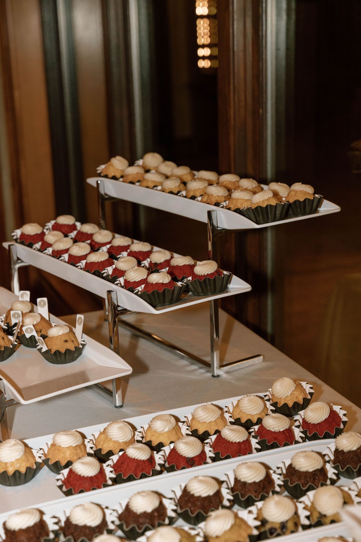 Tiered display of elegant desserts and cupcakes arranged on white serving platters.