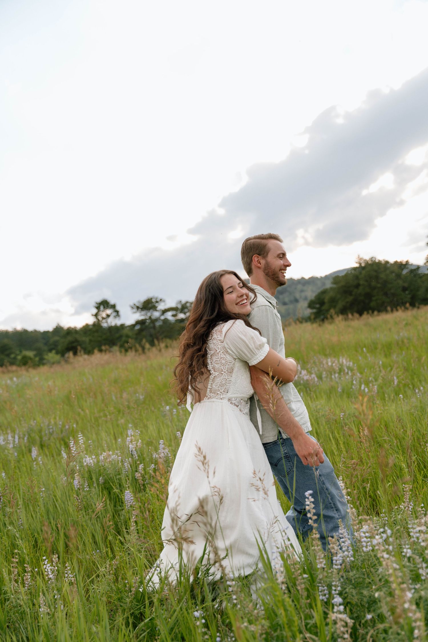 Playful couple spins around in a field of purple wildflowers with mountains visible in the distance.