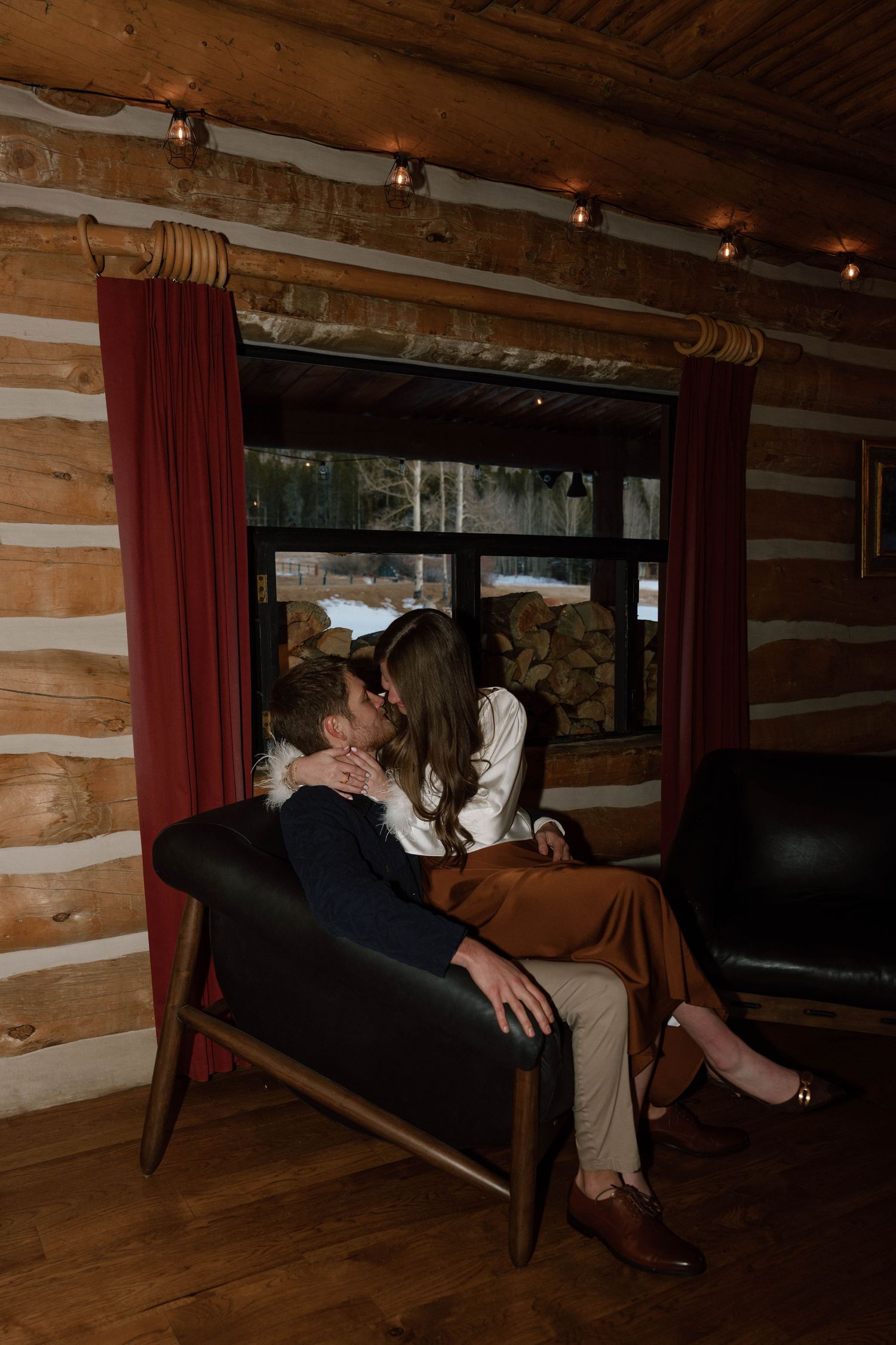 Romantic scene in a rustic log cabin with wooden beams and red curtains.