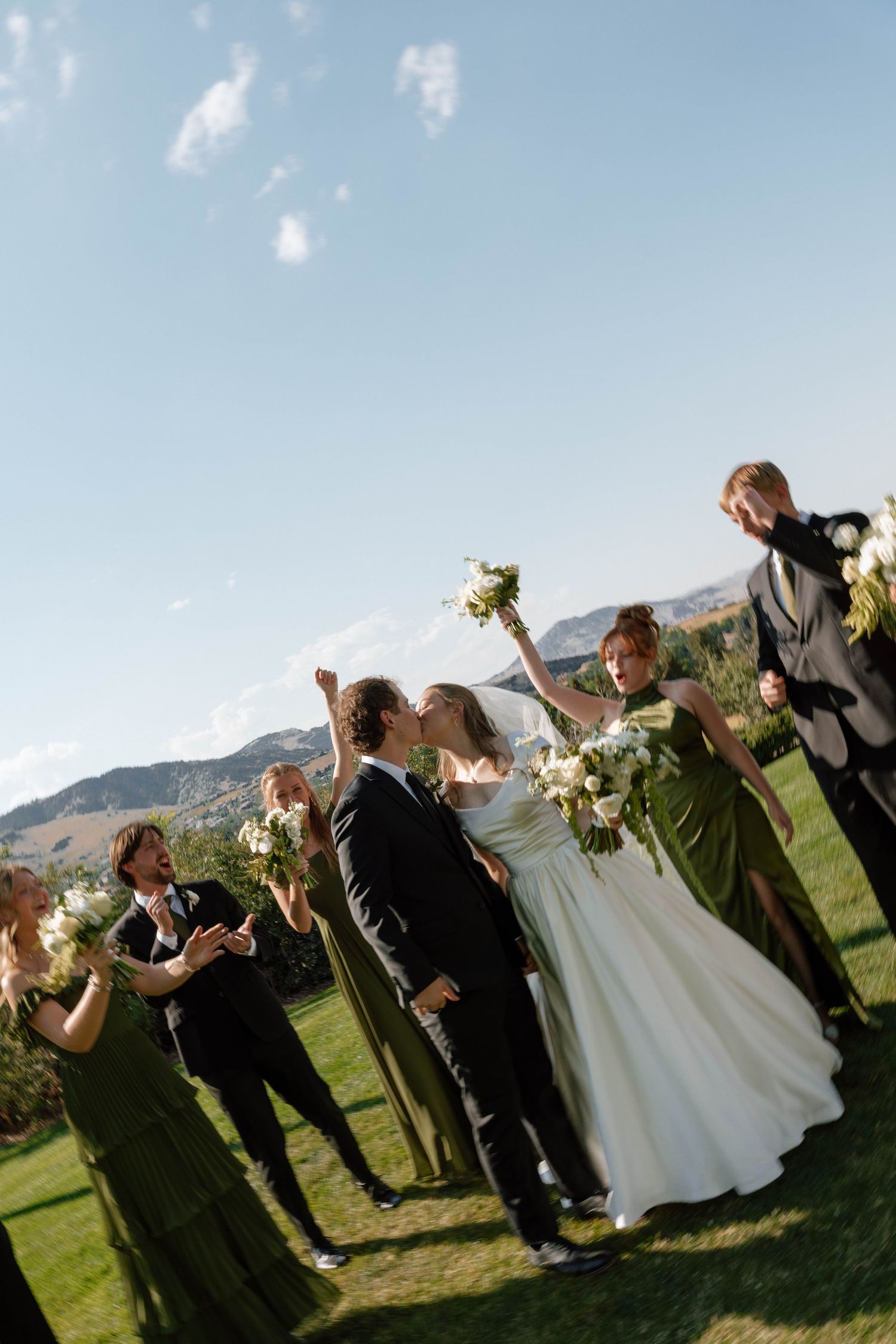 Wedding party celebrates with joyful poses in a scenic outdoor setting with mountain views.