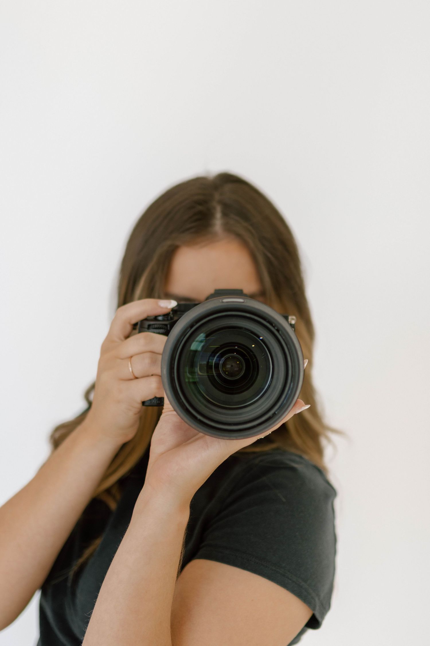 Photographer holding professional camera with large lens against white backdrop.