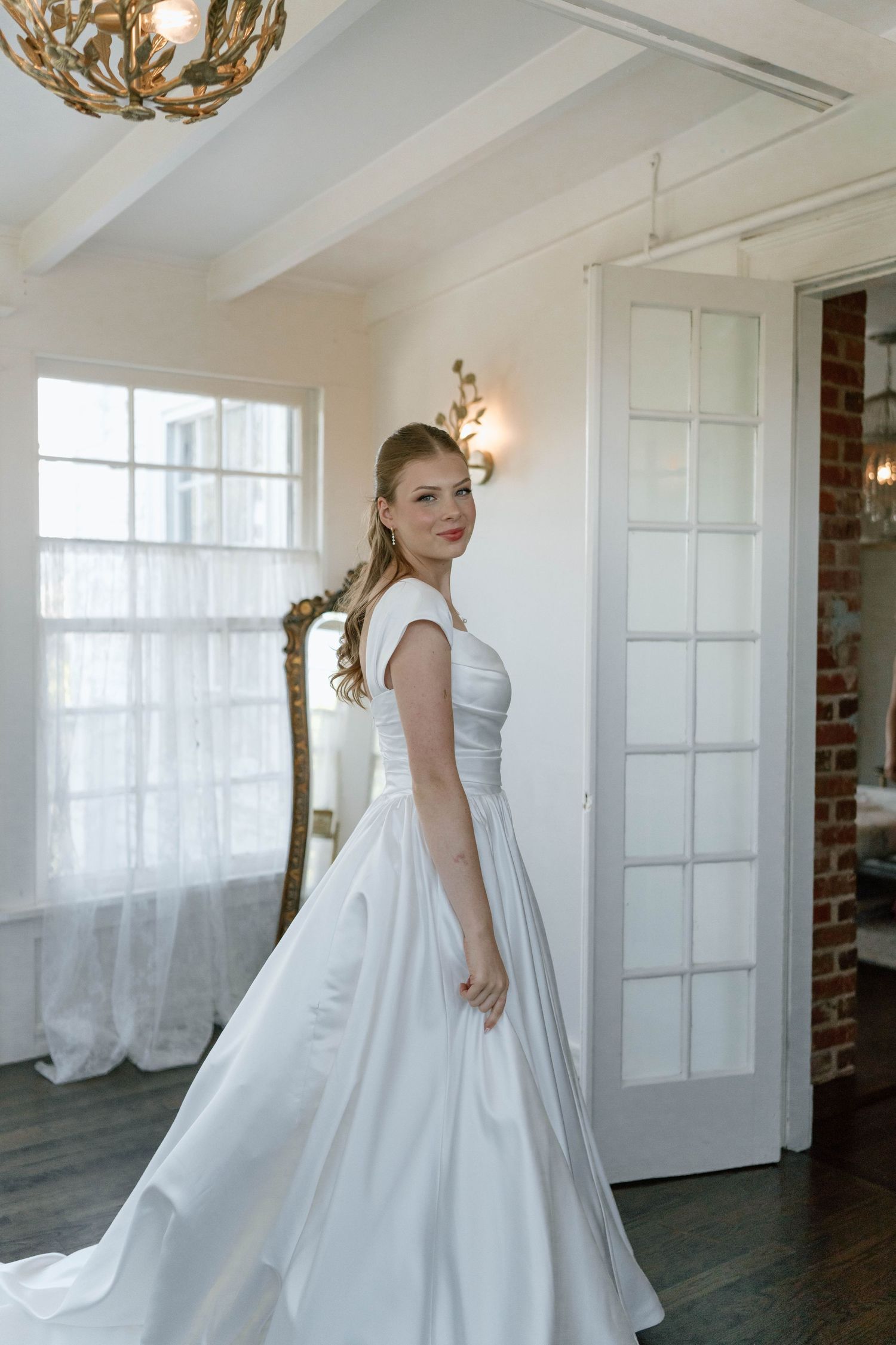 A flowing white dress twirls gracefully in an elegant white studio space with ornate chandelier.