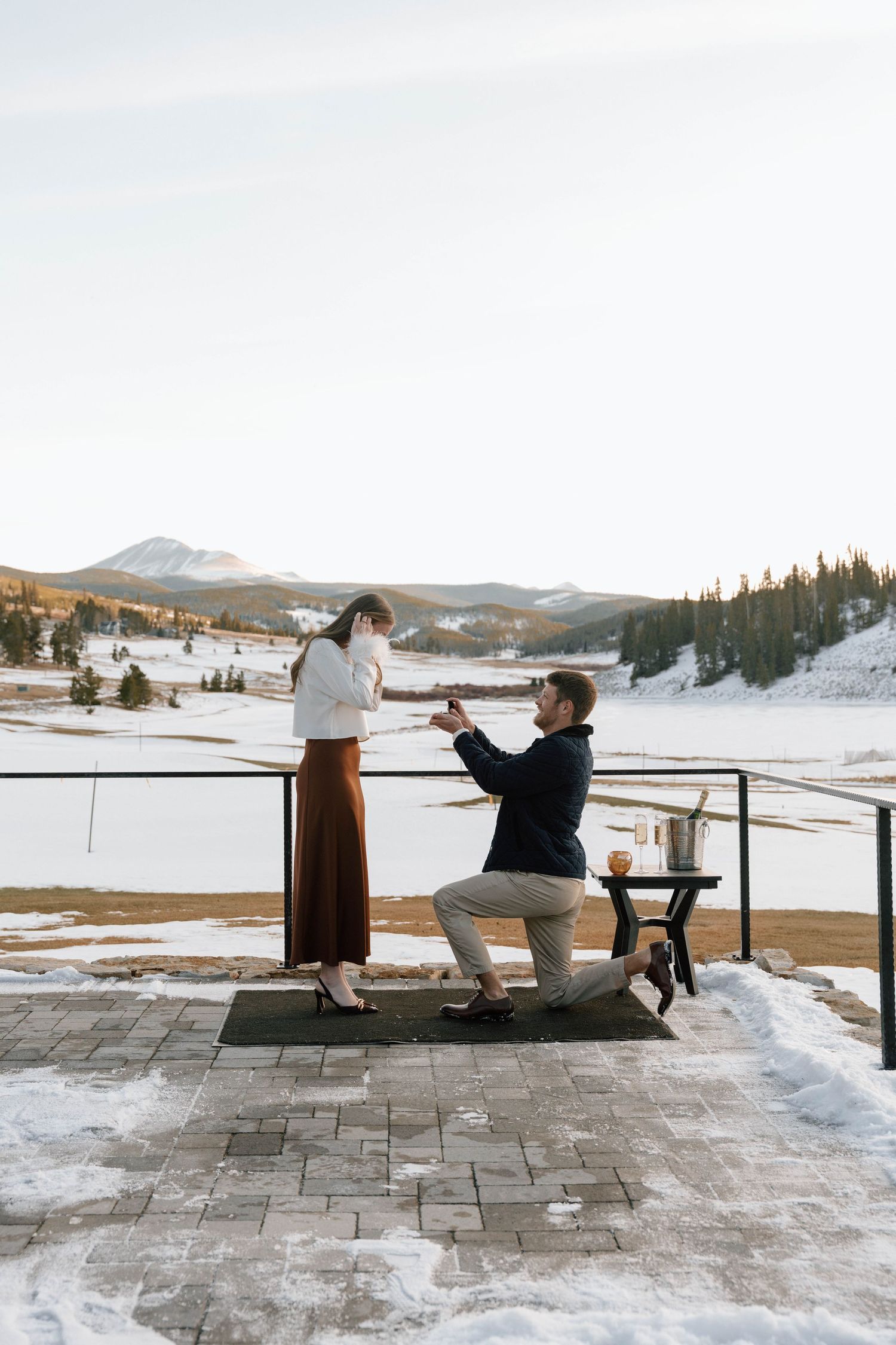Winter proposal moment on mountain deck with scenic snow-covered landscape.