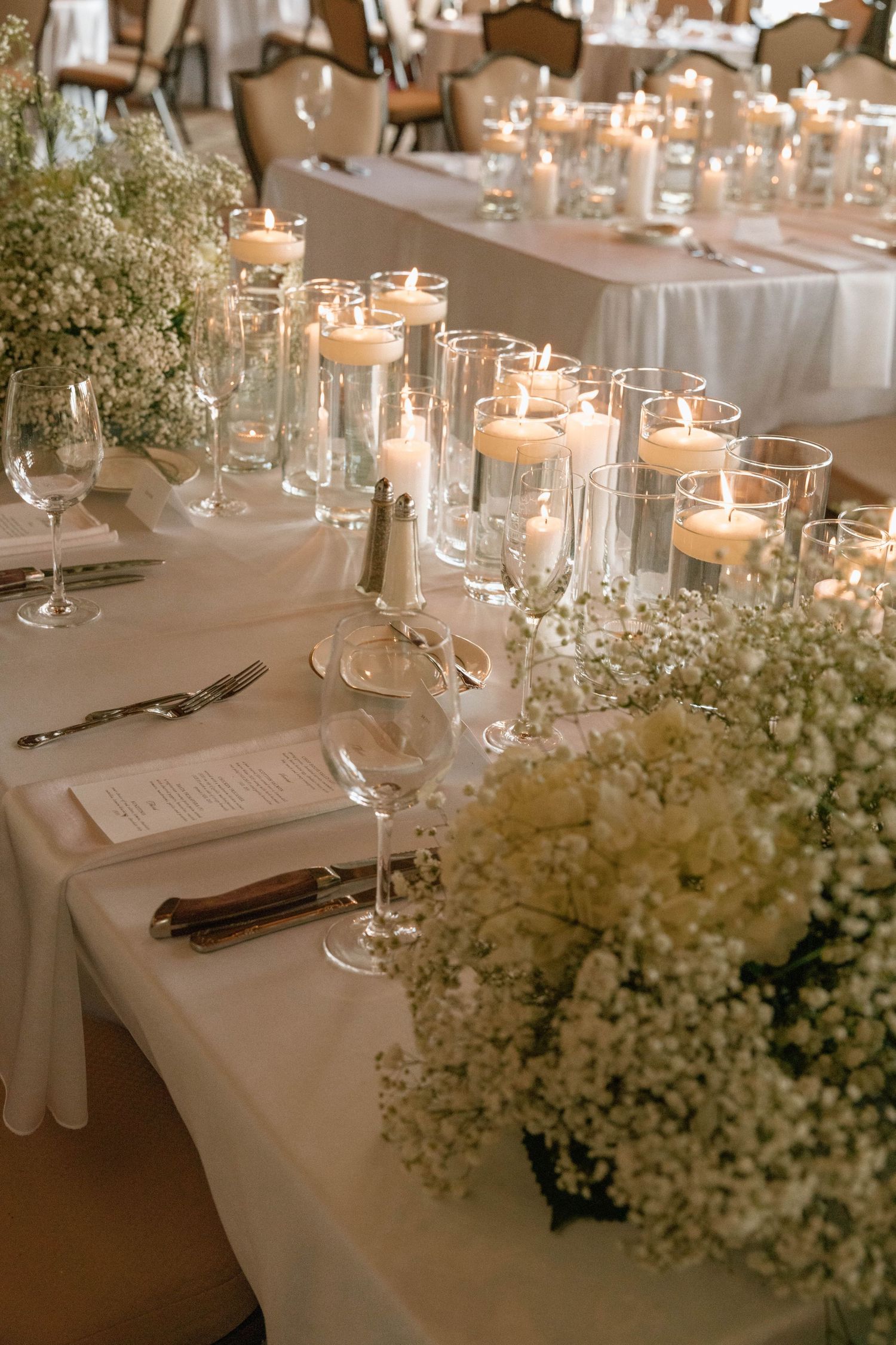 Wedding reception tables decorated with baby's breath centerpieces and floating candles in glass vessels.