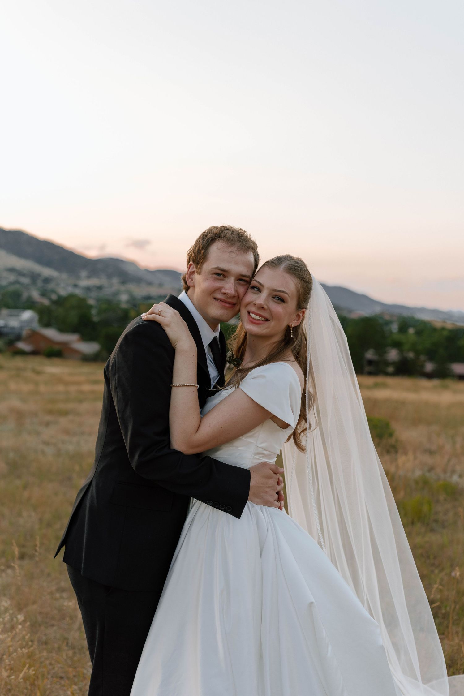 Joyful wedding moment captured in mountain field during sunset.