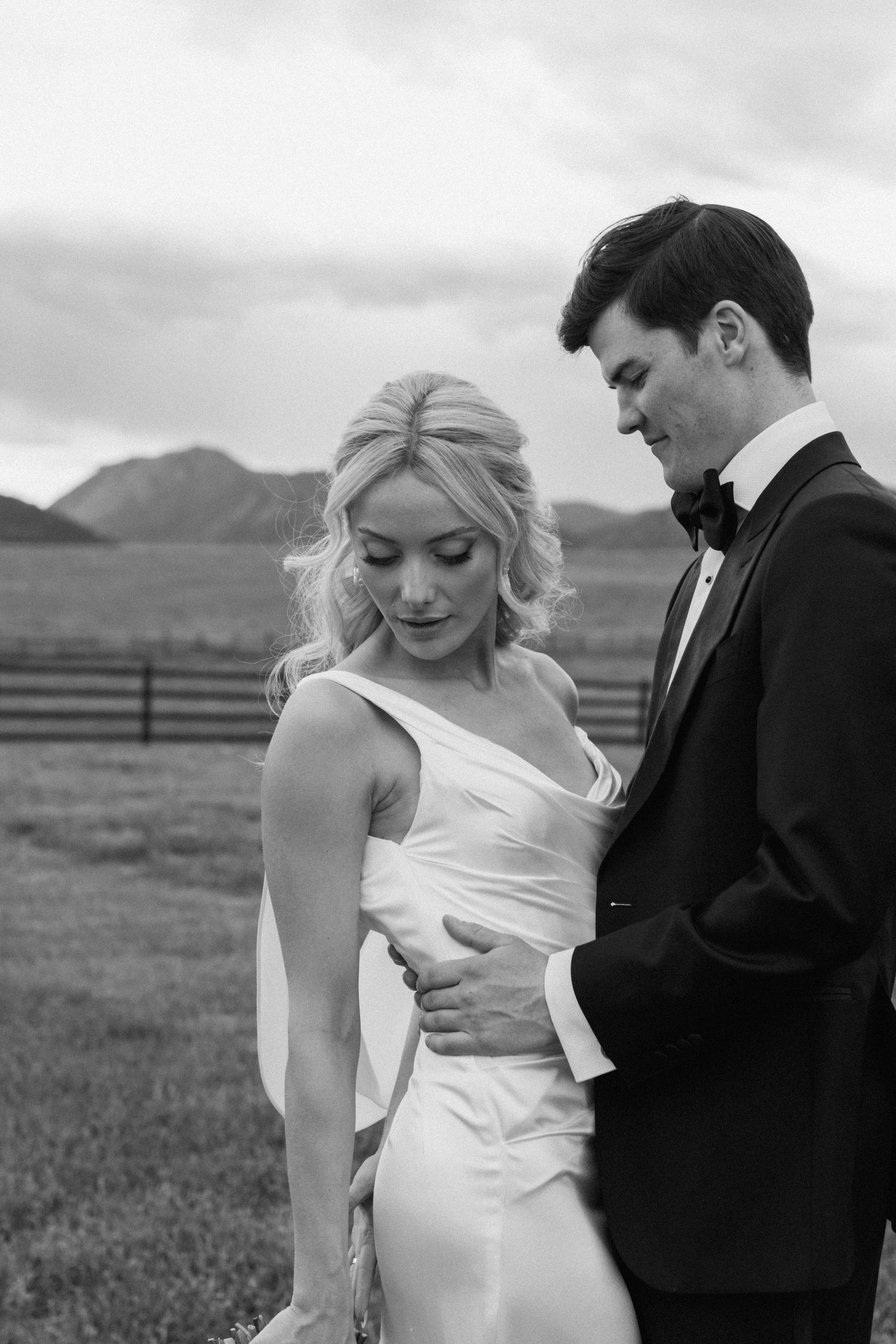 Black and white photo of a bride and groom sharing a tender moment outdoors with mountains in the background.