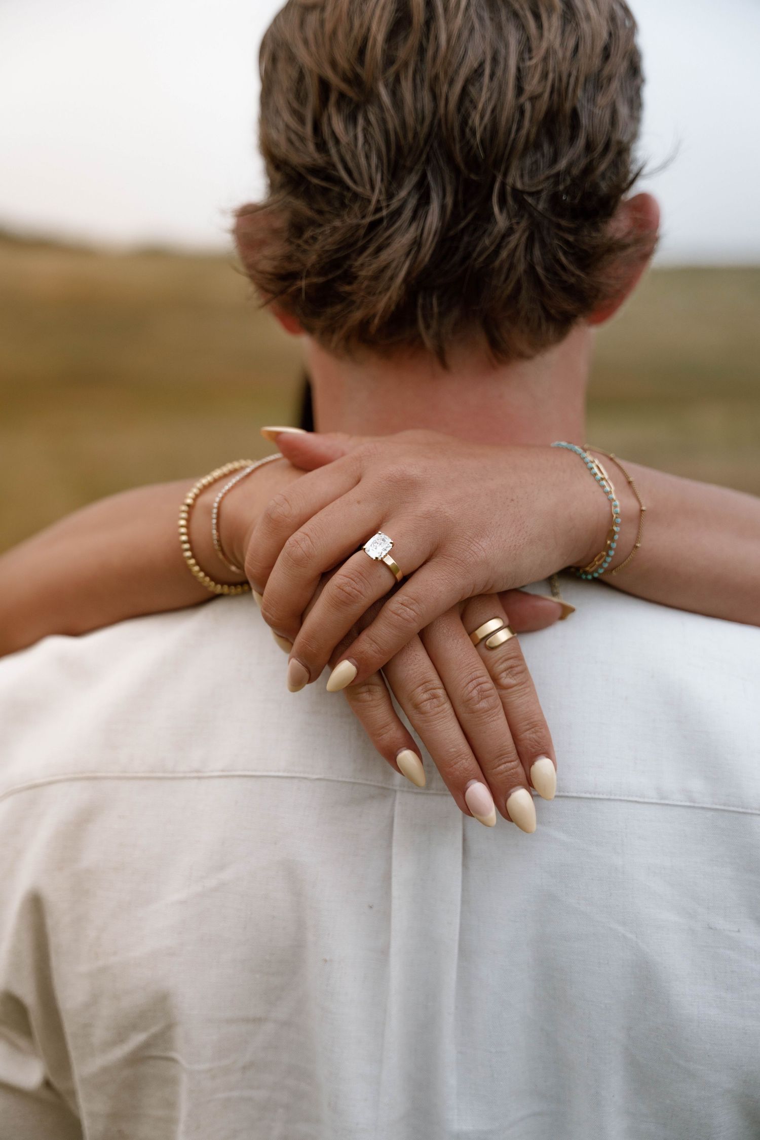 Close-up of hands resting on shoulders showing wedding rings and white clothing details.